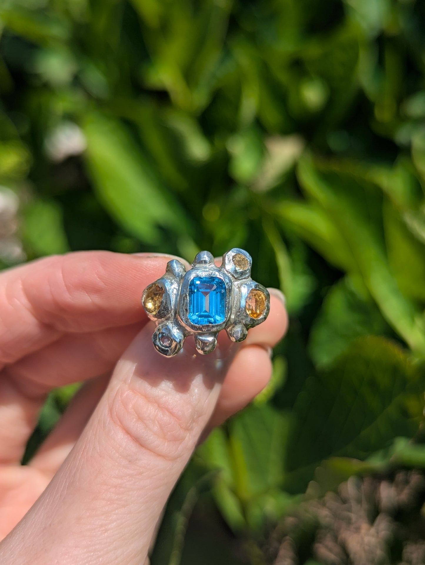 Bohemian Silver Ring with a blue and yellow gemstones held by a hand against a green leafy background
