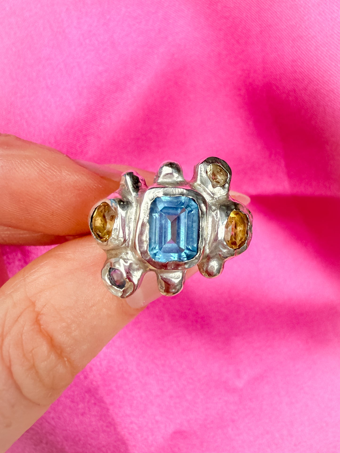 Bohemian silver ring with blue and yellow gemstones held by a hand against a pink background