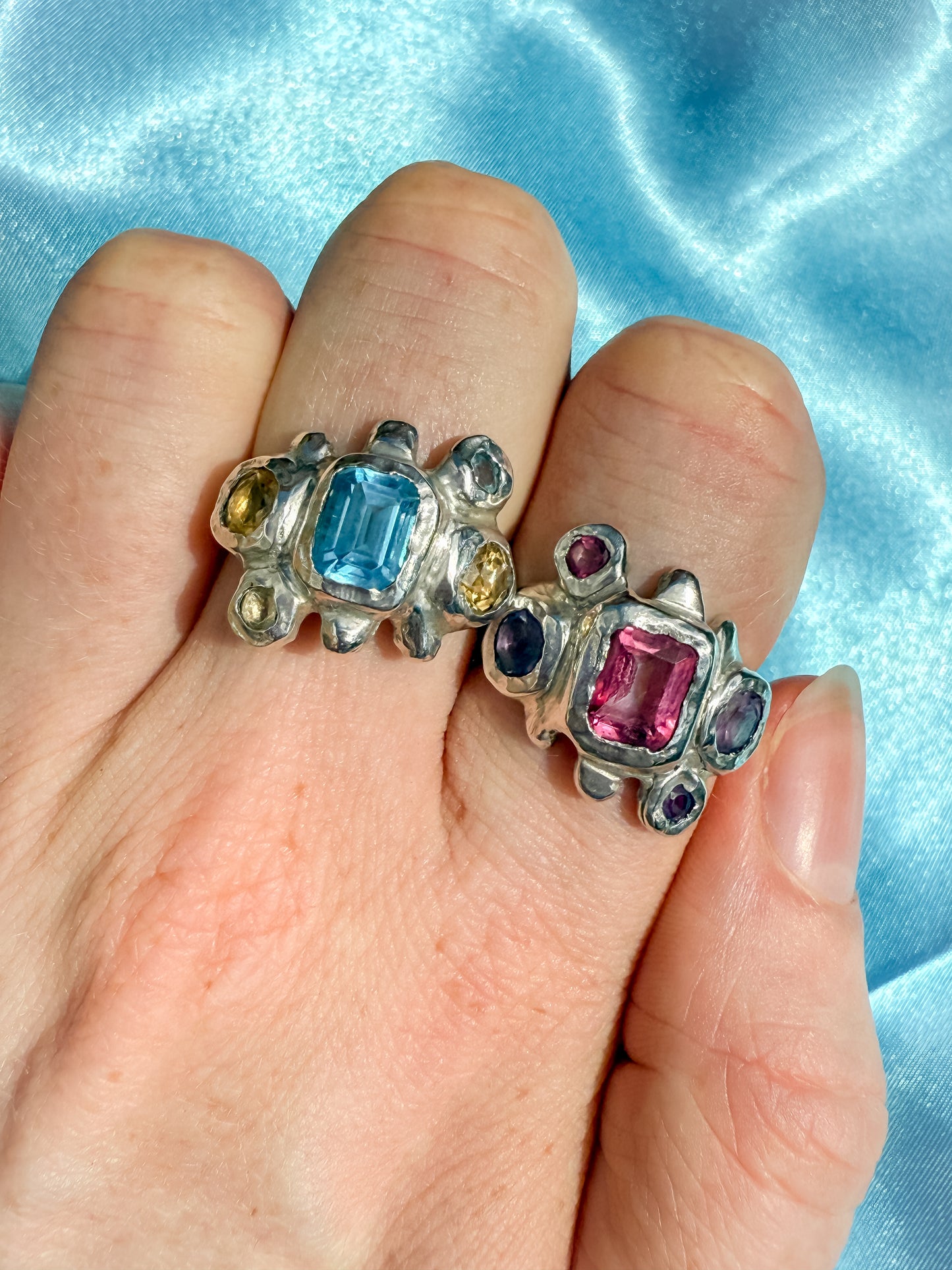 Two silver bohemian rings with blue, yellow, pink and purple gemstones against blue background