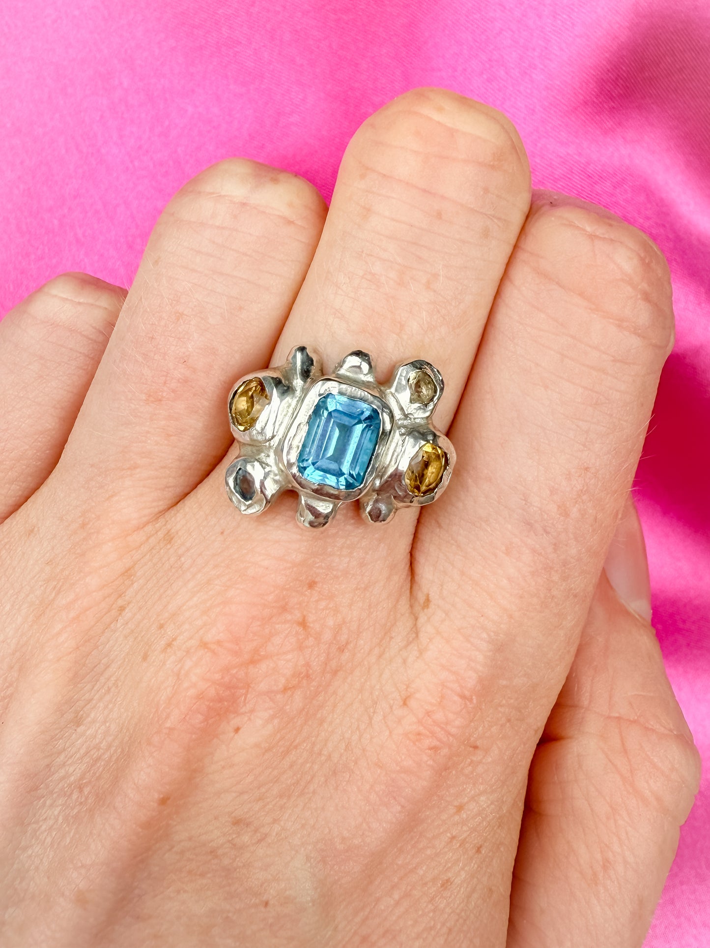 Silver bohemian ring with blue gemstone and yellow stones on a hand against a pink background