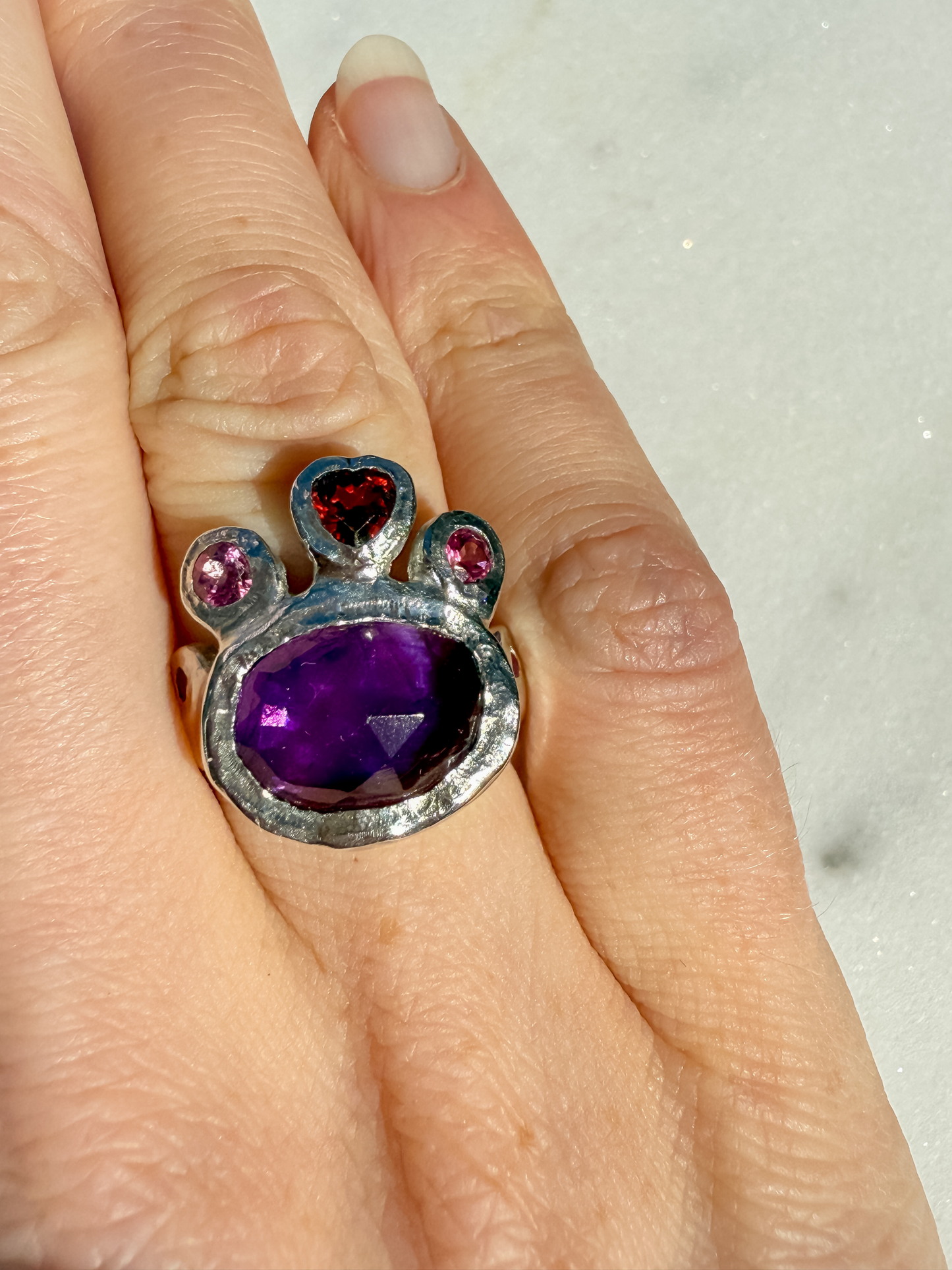 Ring with purple gemstone and heart-shaped pink and red stones on a hand