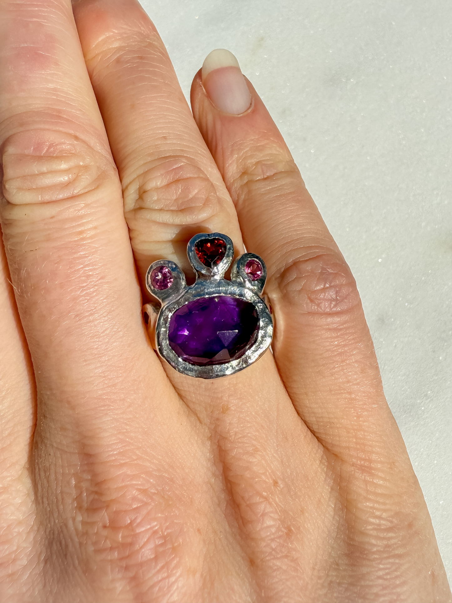 Ring with purple gemstone on a hand against a white background