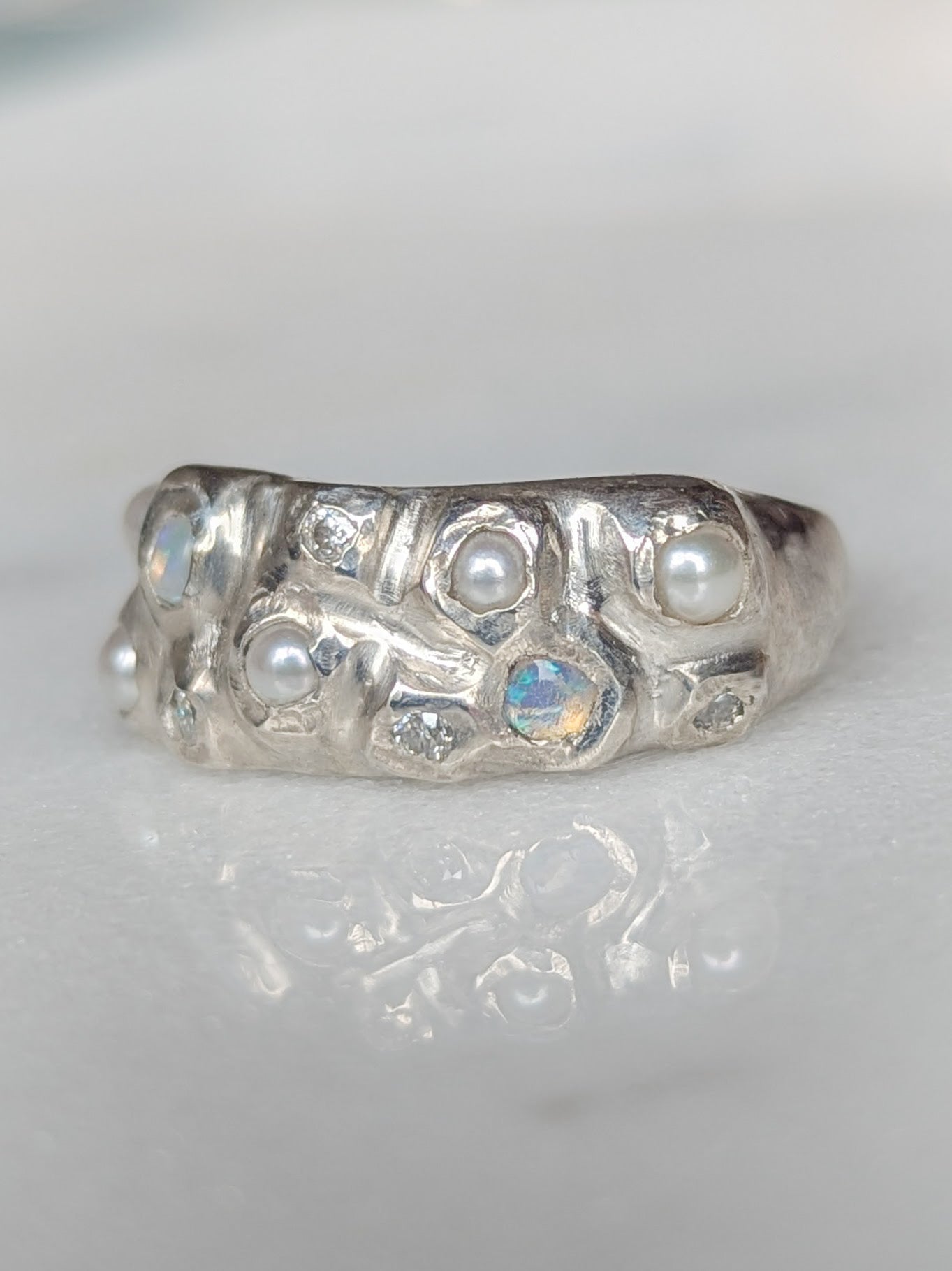 Silver ring with embedded pearls, opals and moissanite gemstones on a white background