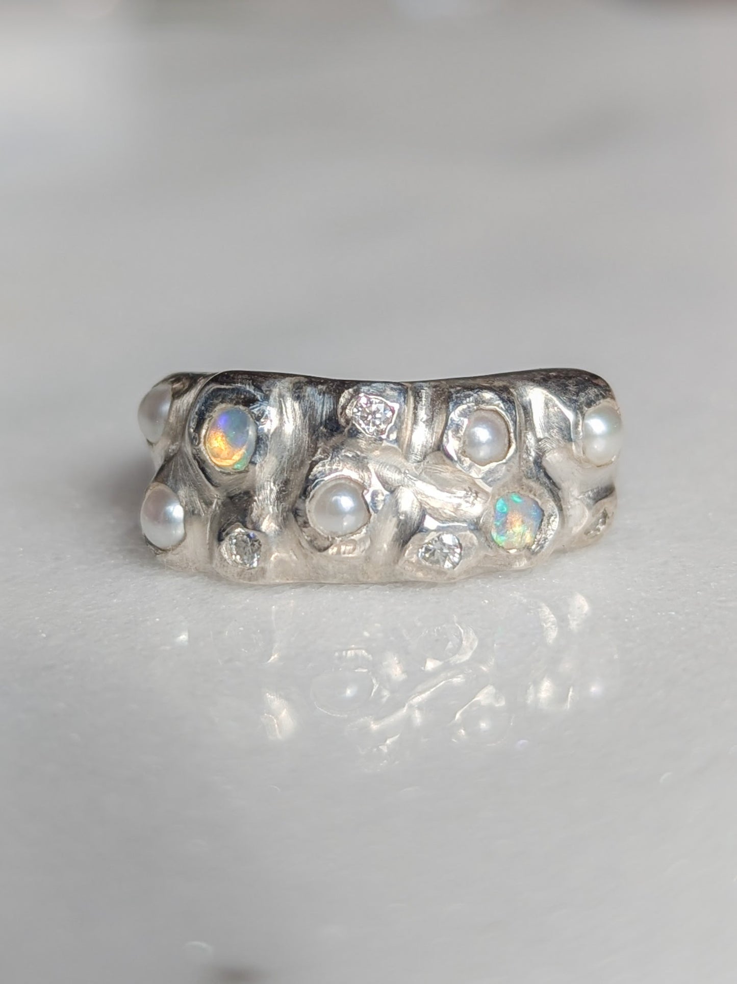 Silver ring with embedded pearls, opals and moissanite gemstones on a white background