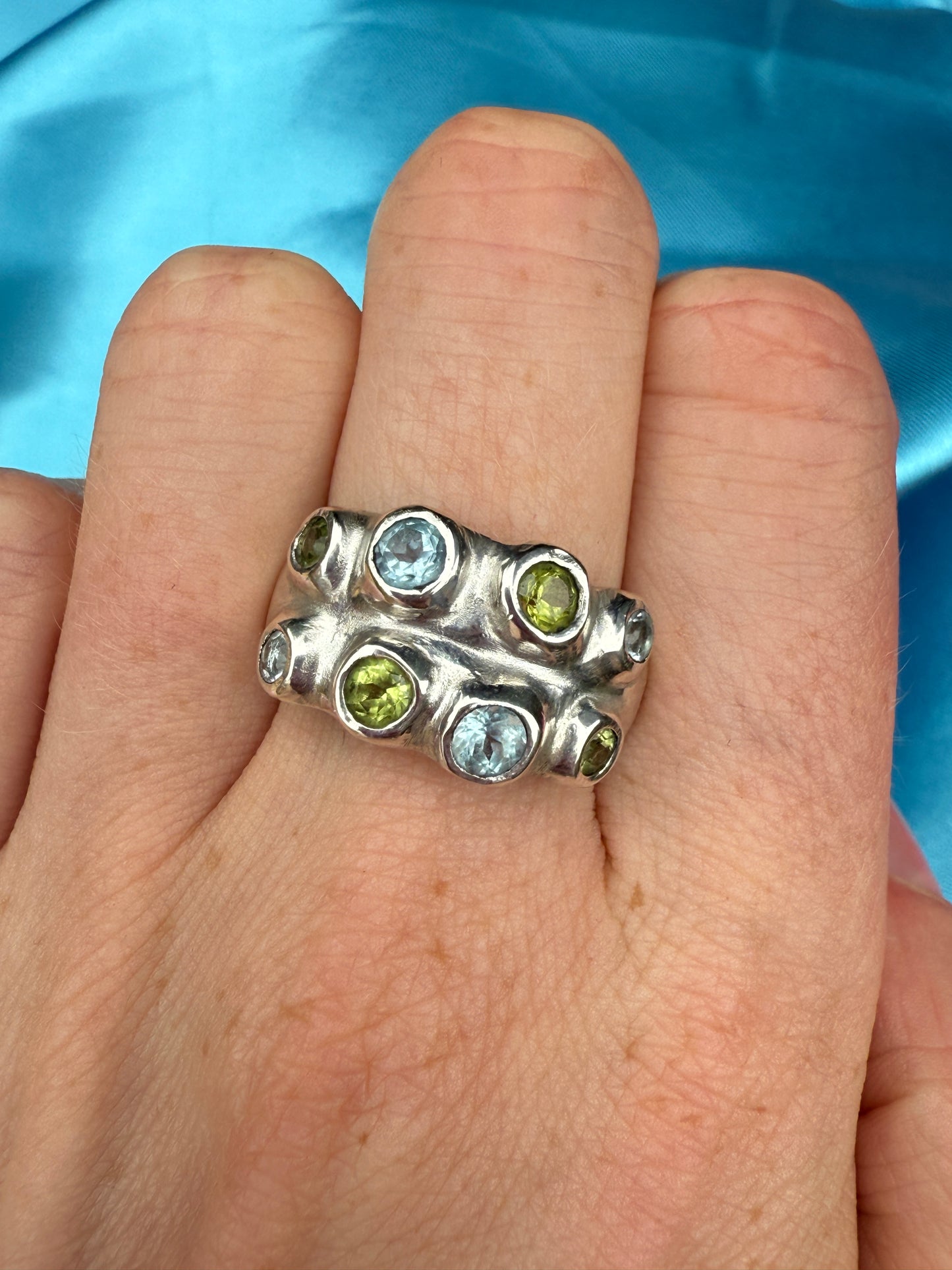 Silver ring with blue and green stones on a hand against a blue background
