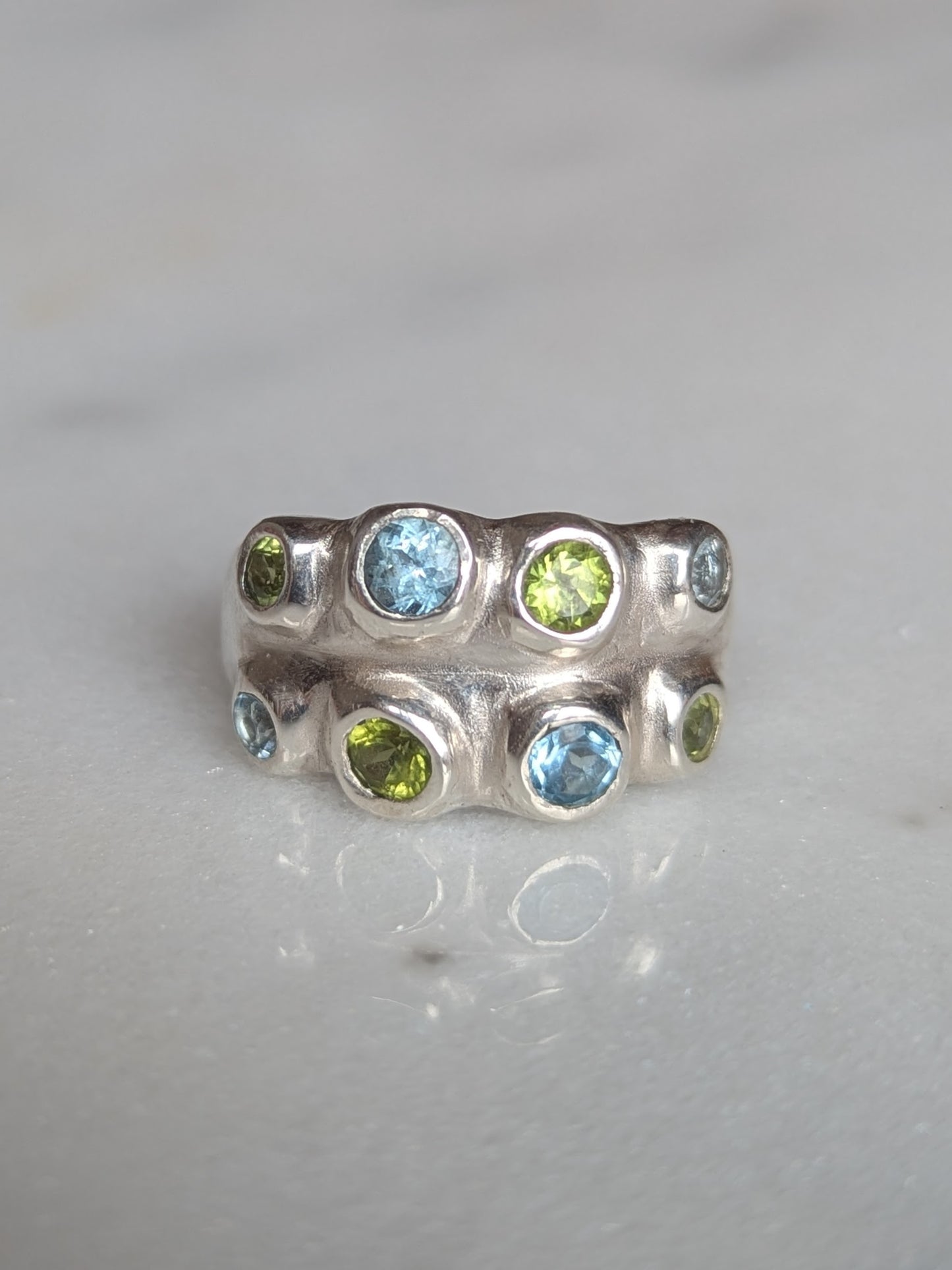 Silver ring with green and blue gemstones on a light gray background