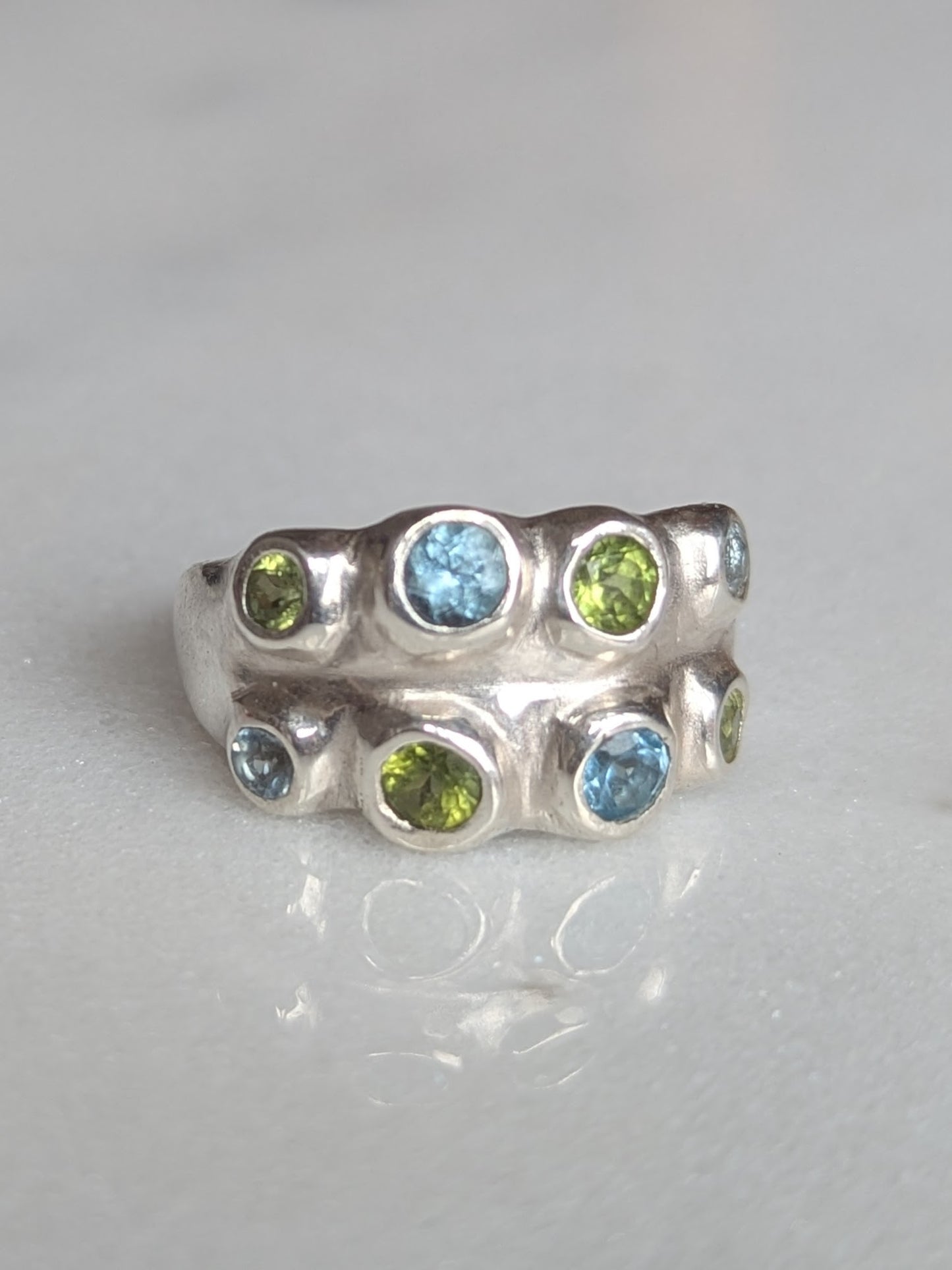 Silver ring with green and blue gemstones on a gray background