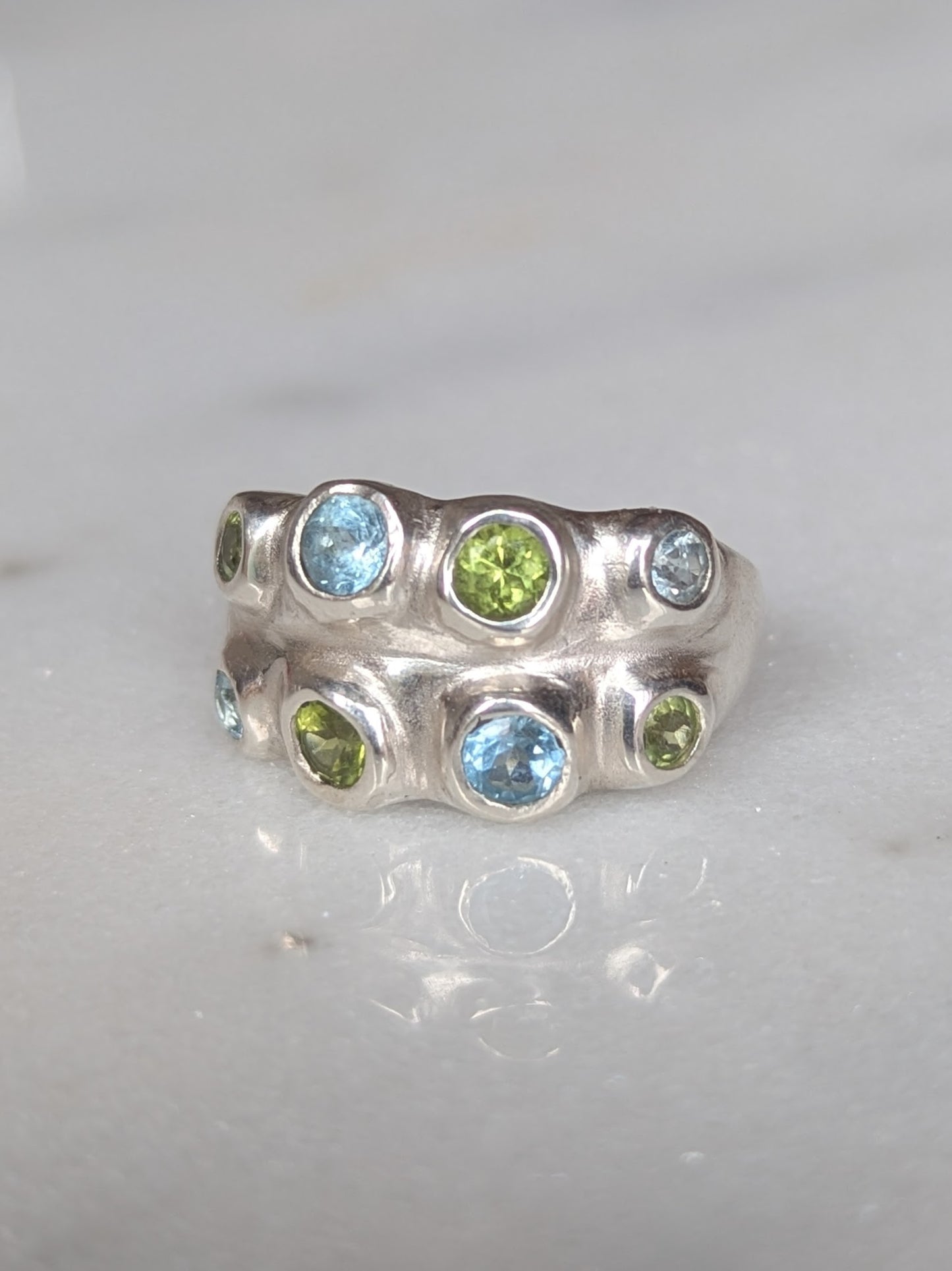 Silver ring with blue and green gemstones on a white background
