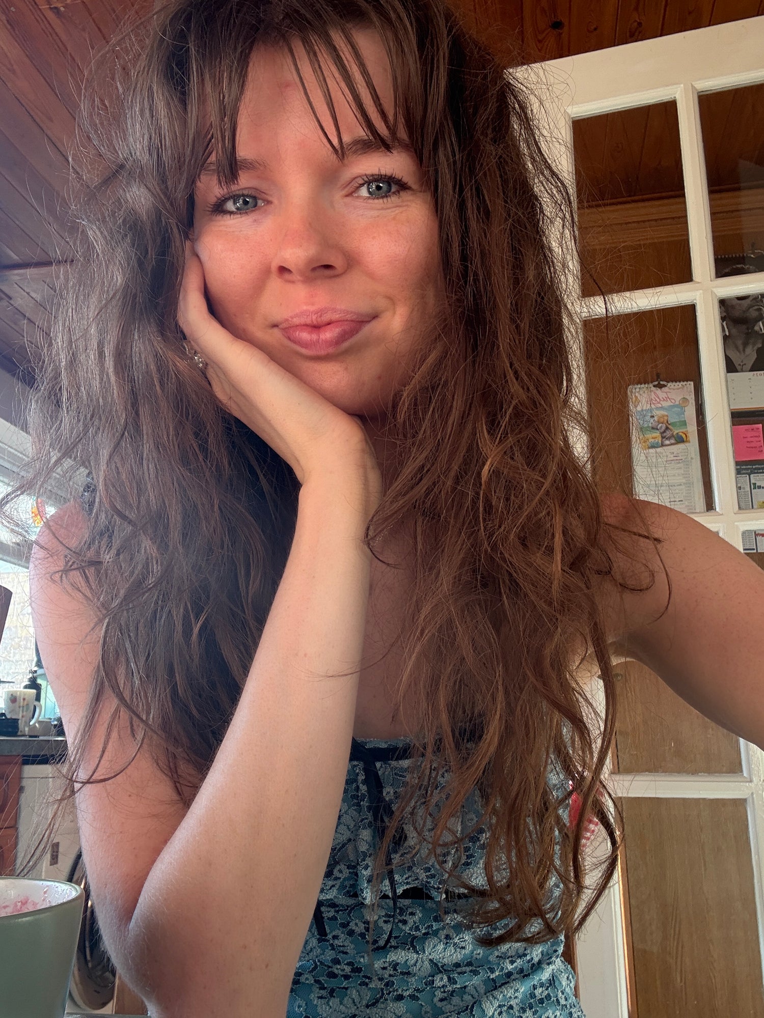 Woman with long hair posing indoors with a wooden floor and furniture in the background
