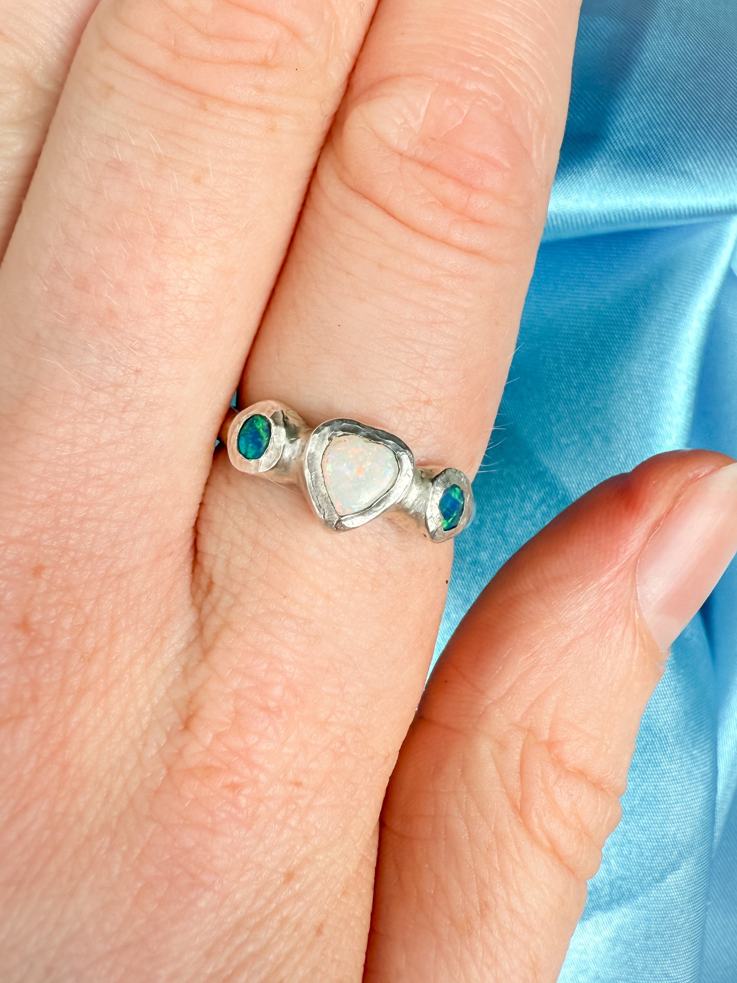 Silver ring with heart design on a person's finger against a blue fabric background