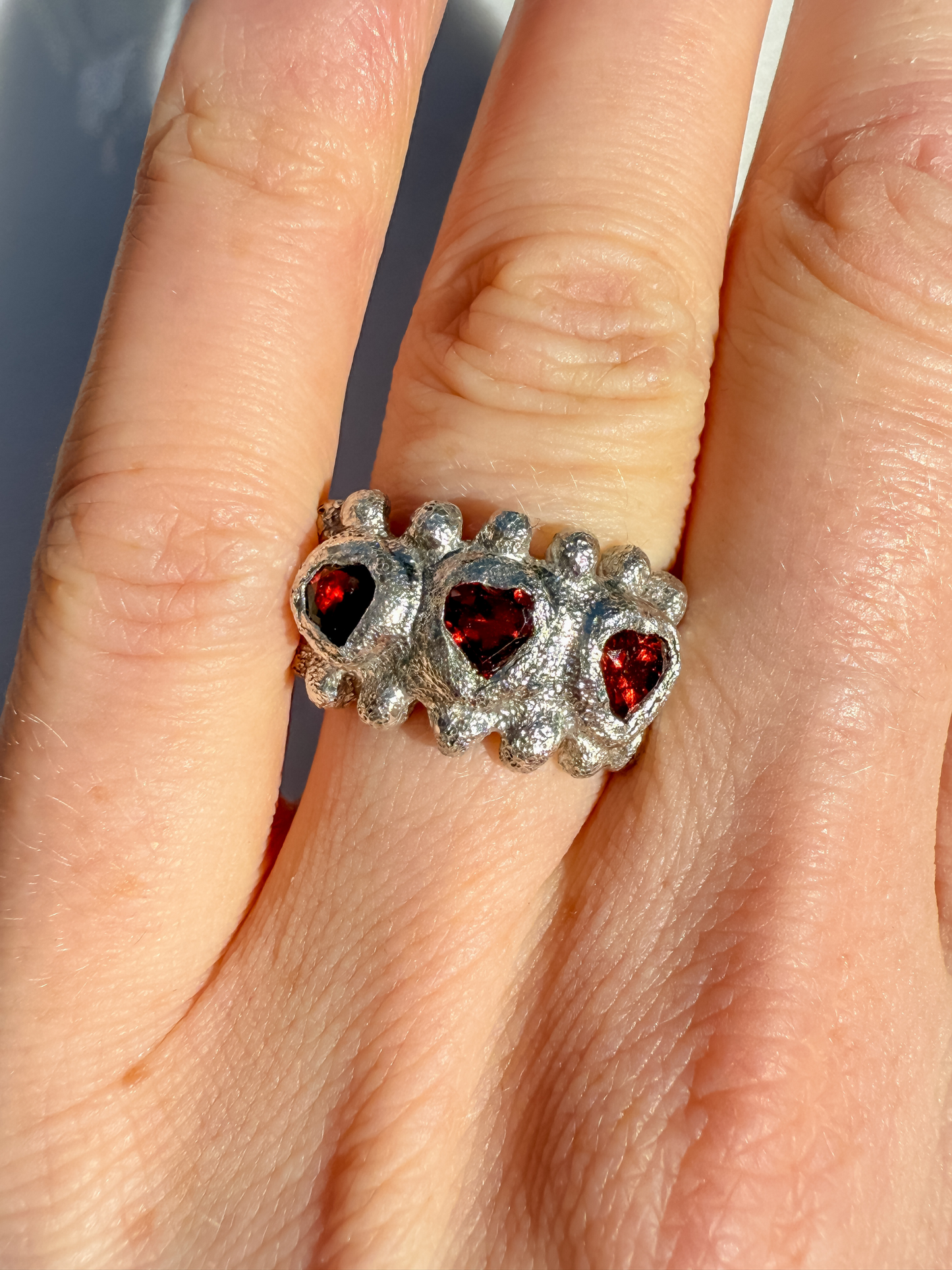 Silver ring with red heart gemstones on a finger