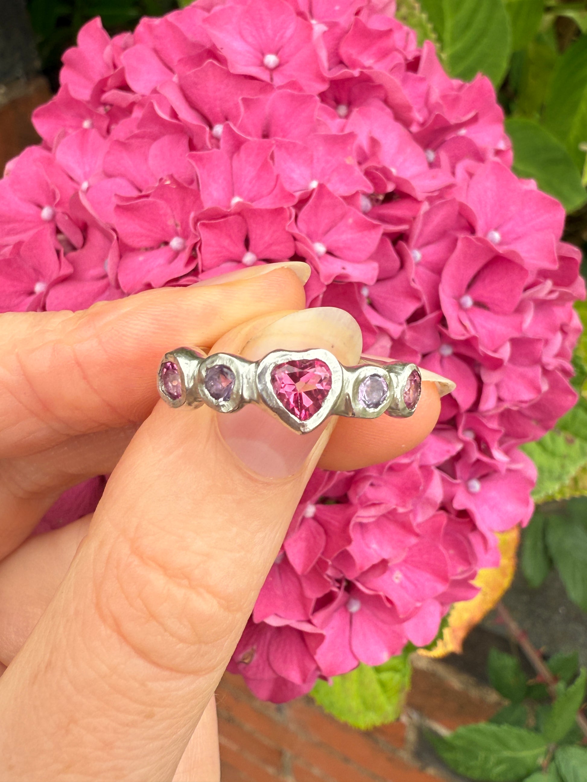 Silver ring with heart gemstones against pink hydrangea background