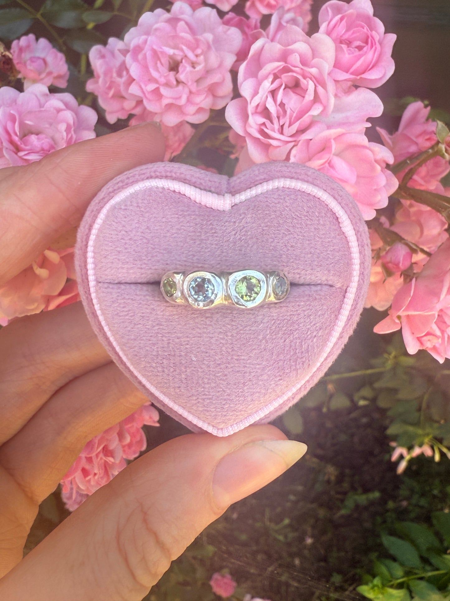 Heart-shaped ring box with a ring inside, held by a hand with pink flowers in the background