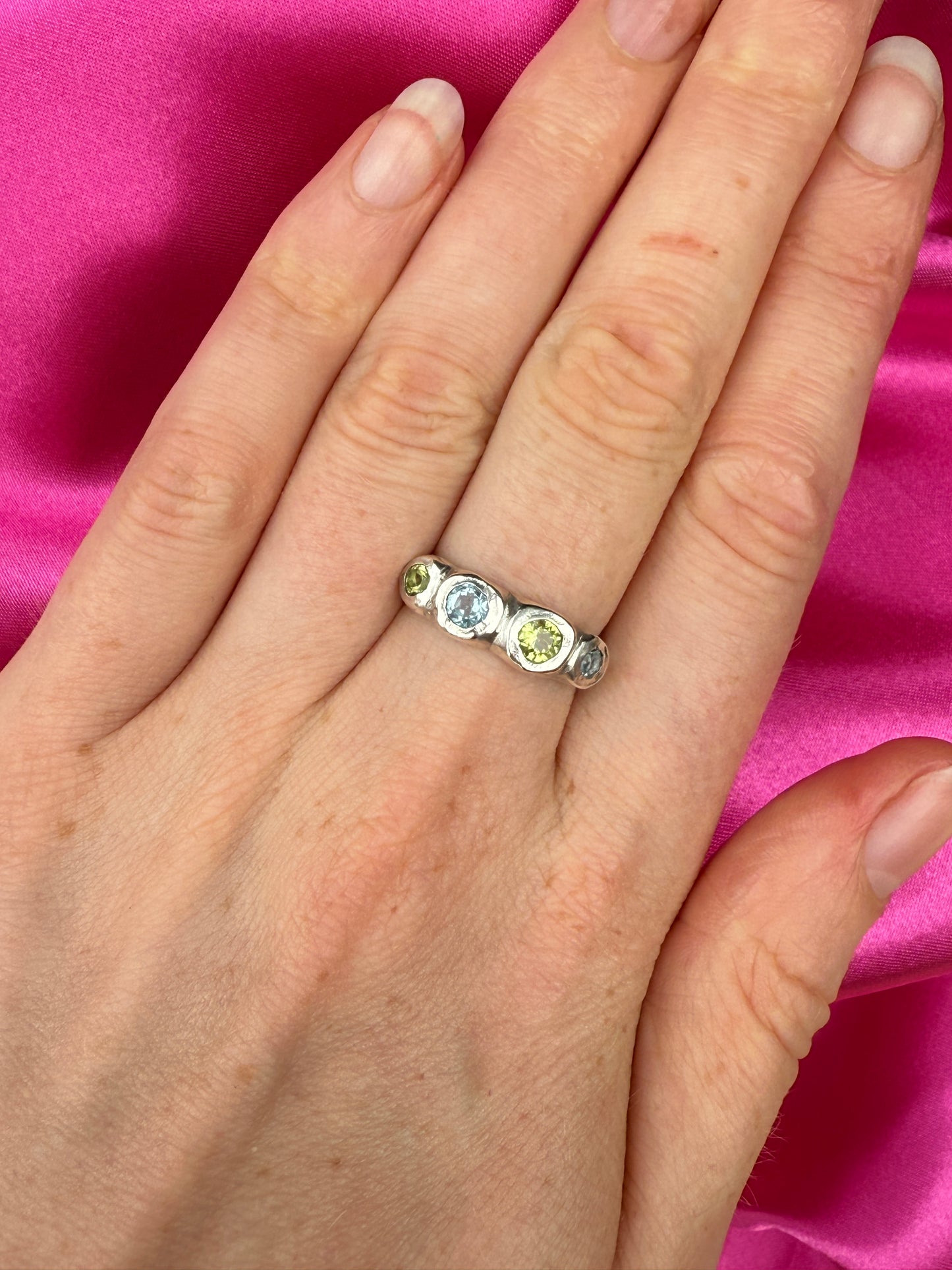 Hand wearing a silver bohemian ring with blue and green gemstones against a pink background