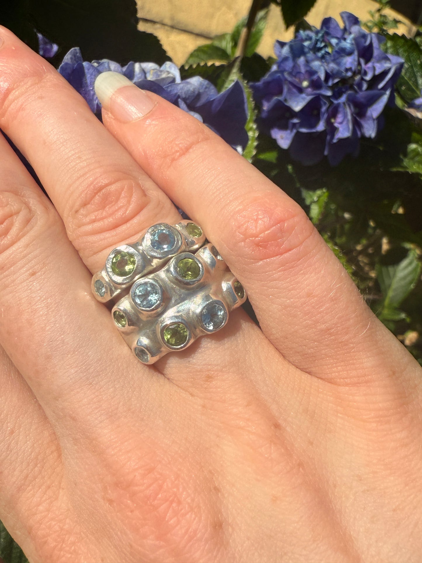 Silver rings with blue and green gemstones with blue hydrangea in background