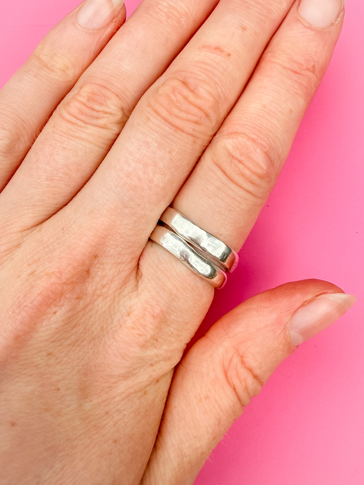 Hand wearing a silver ring on a pink background