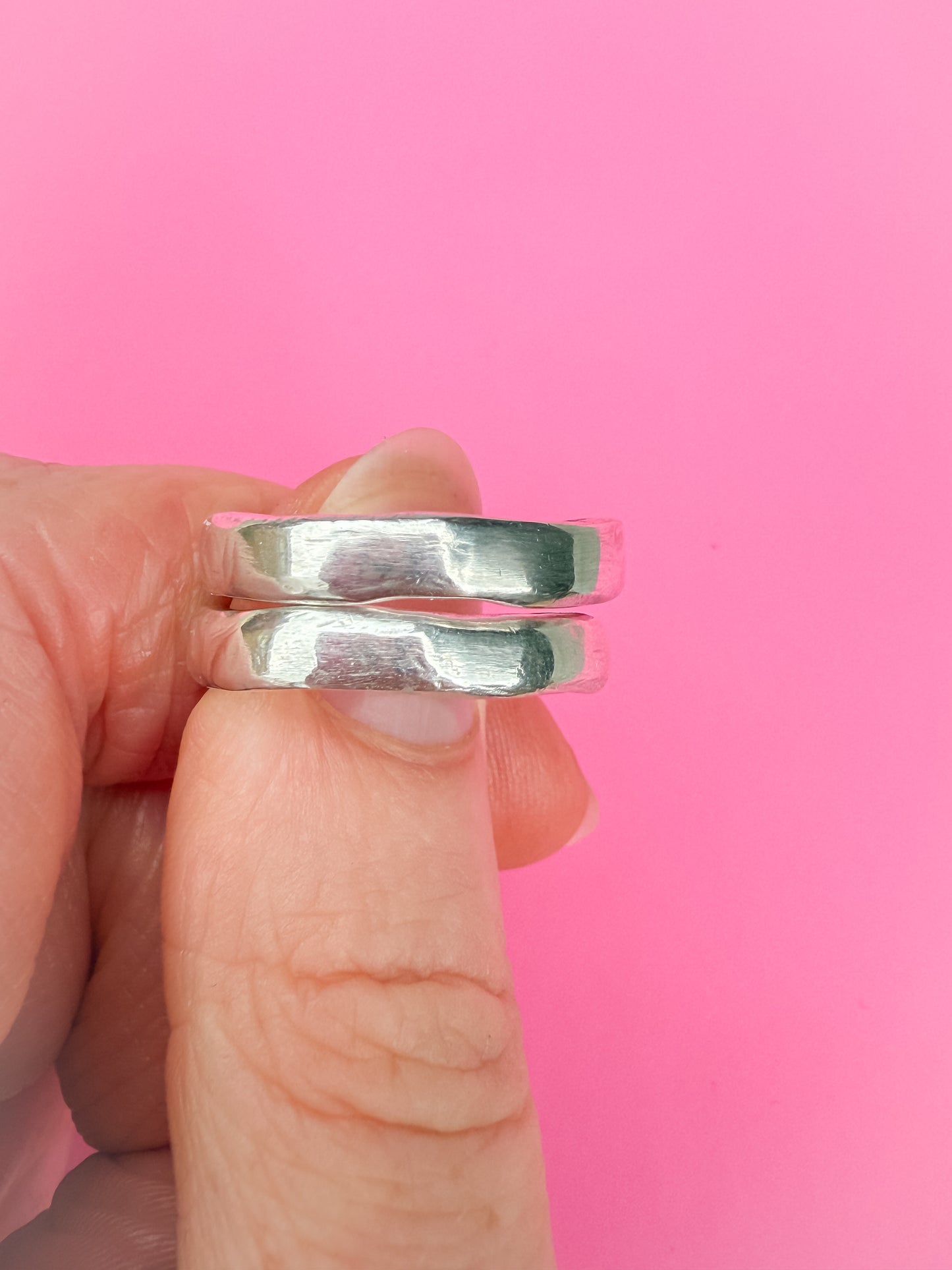 Silver rings held between fingers against a pink background