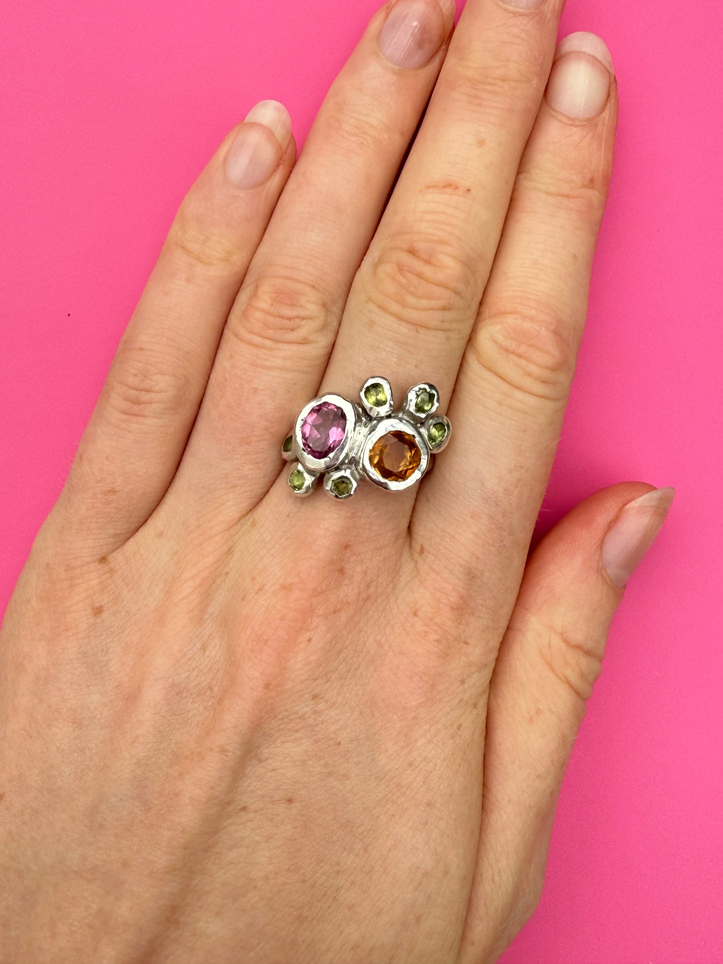 Dreamy silver ring with pink, orange and green gemstones on pink background