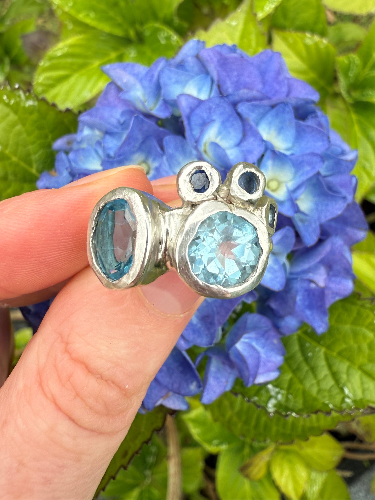 Silver bohemian ring with blue gemstones held against a background of blue flowers and green leaves