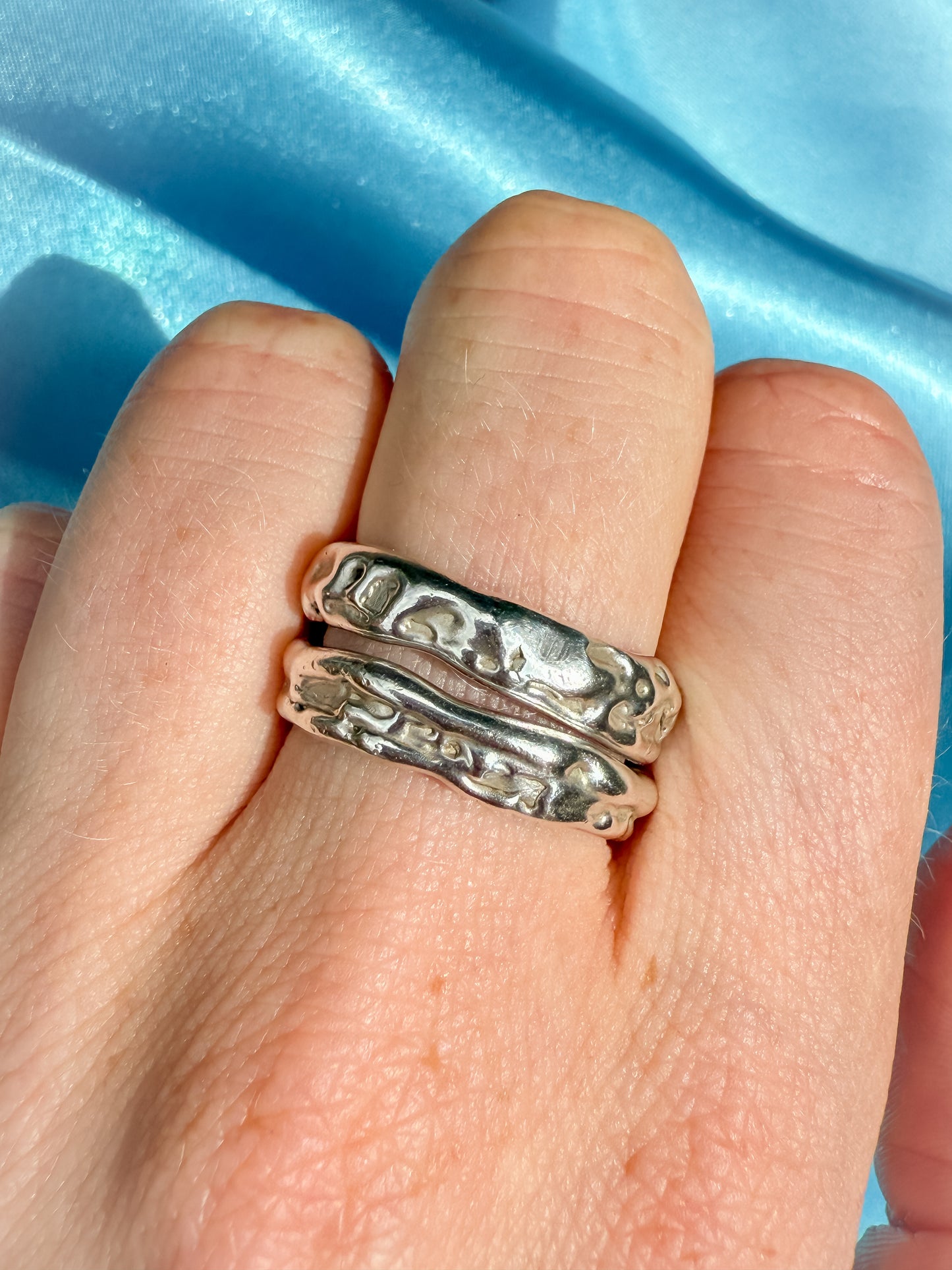 Silver molten ring on a finger against a blue fabric background