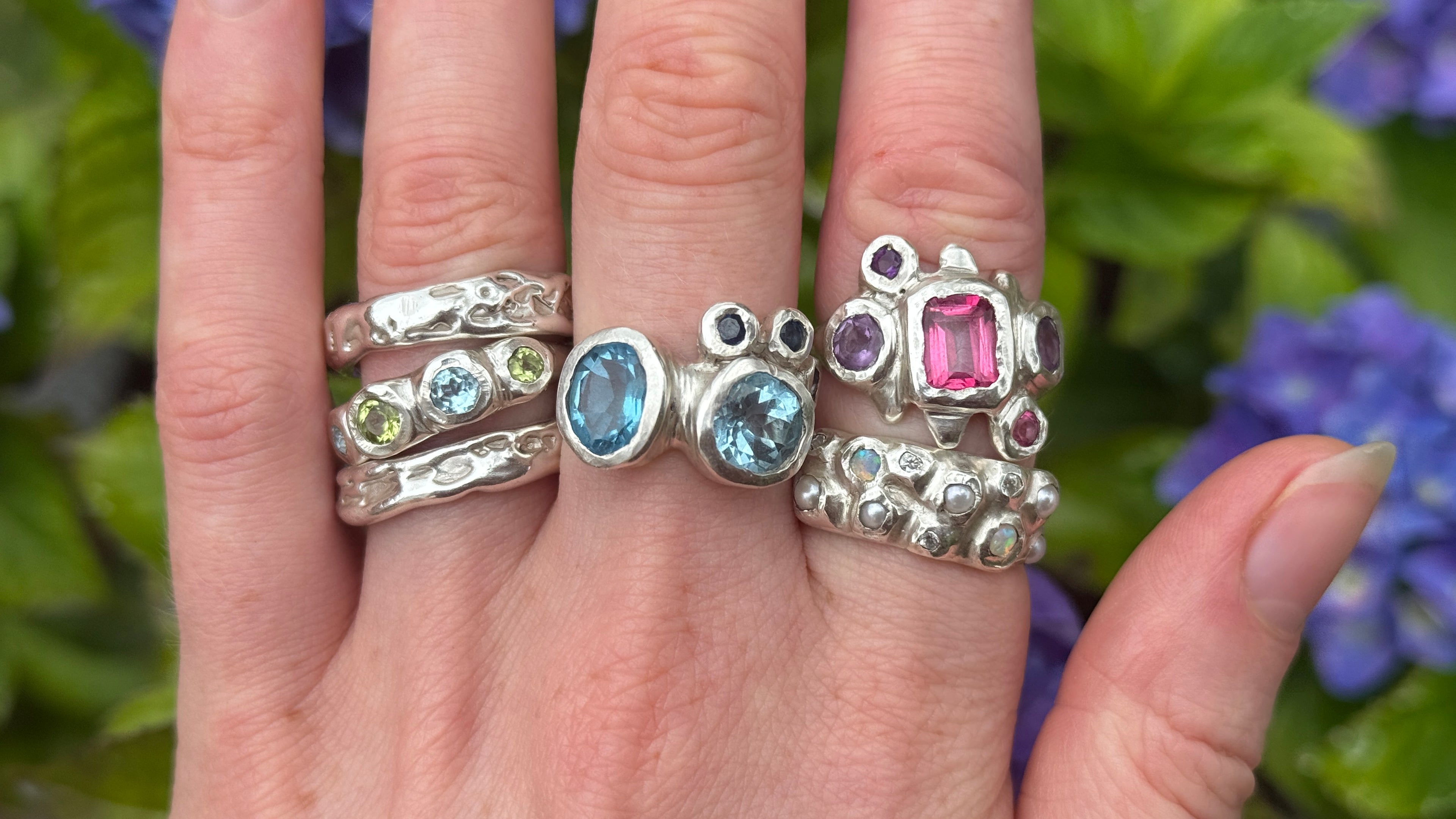 Hand wearing multiple silver rings with gemstones against a floral background