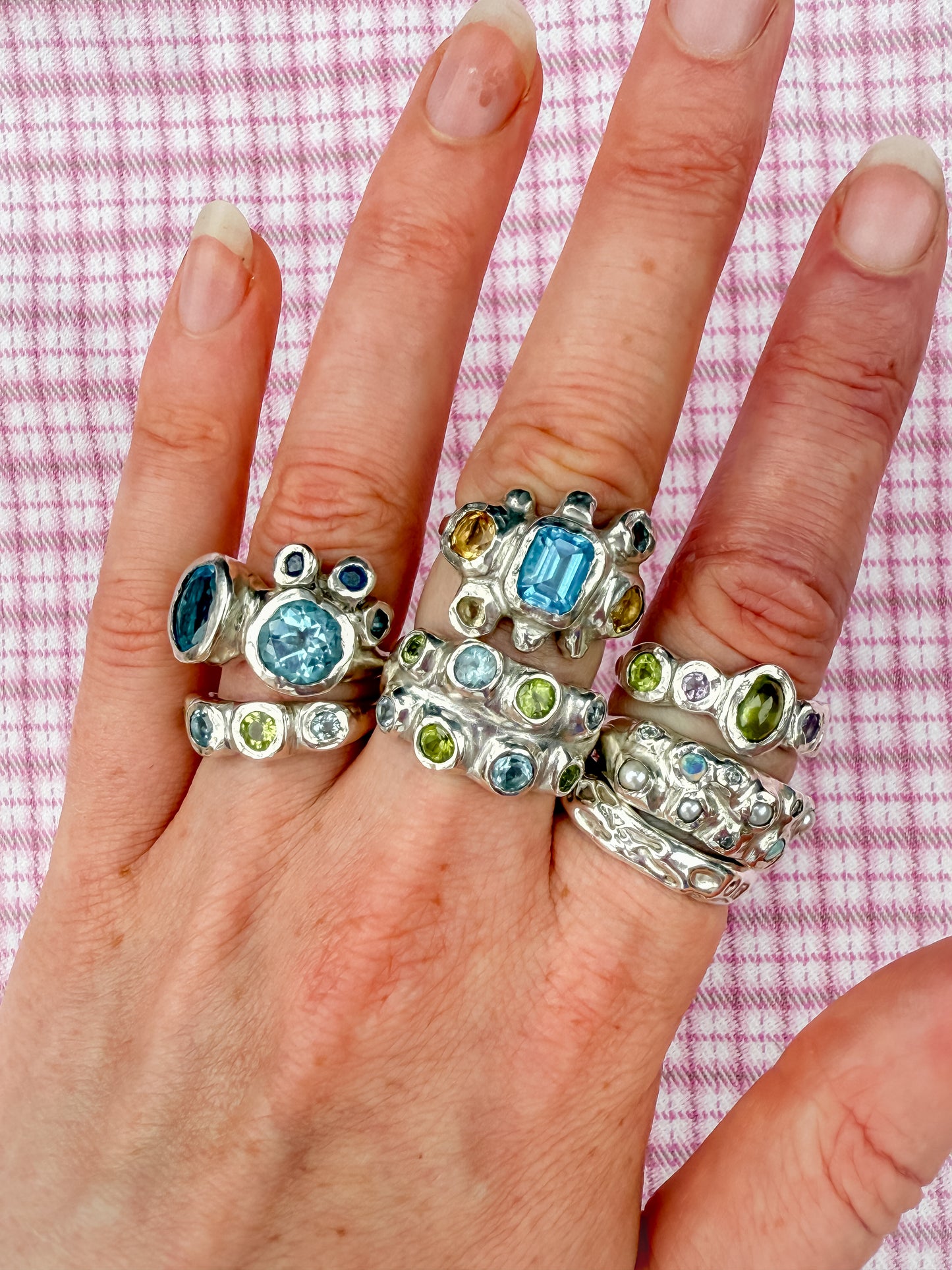 Dreamy silver rings with blue, green, yellow gemstones, opals and pearls on pink checkered background