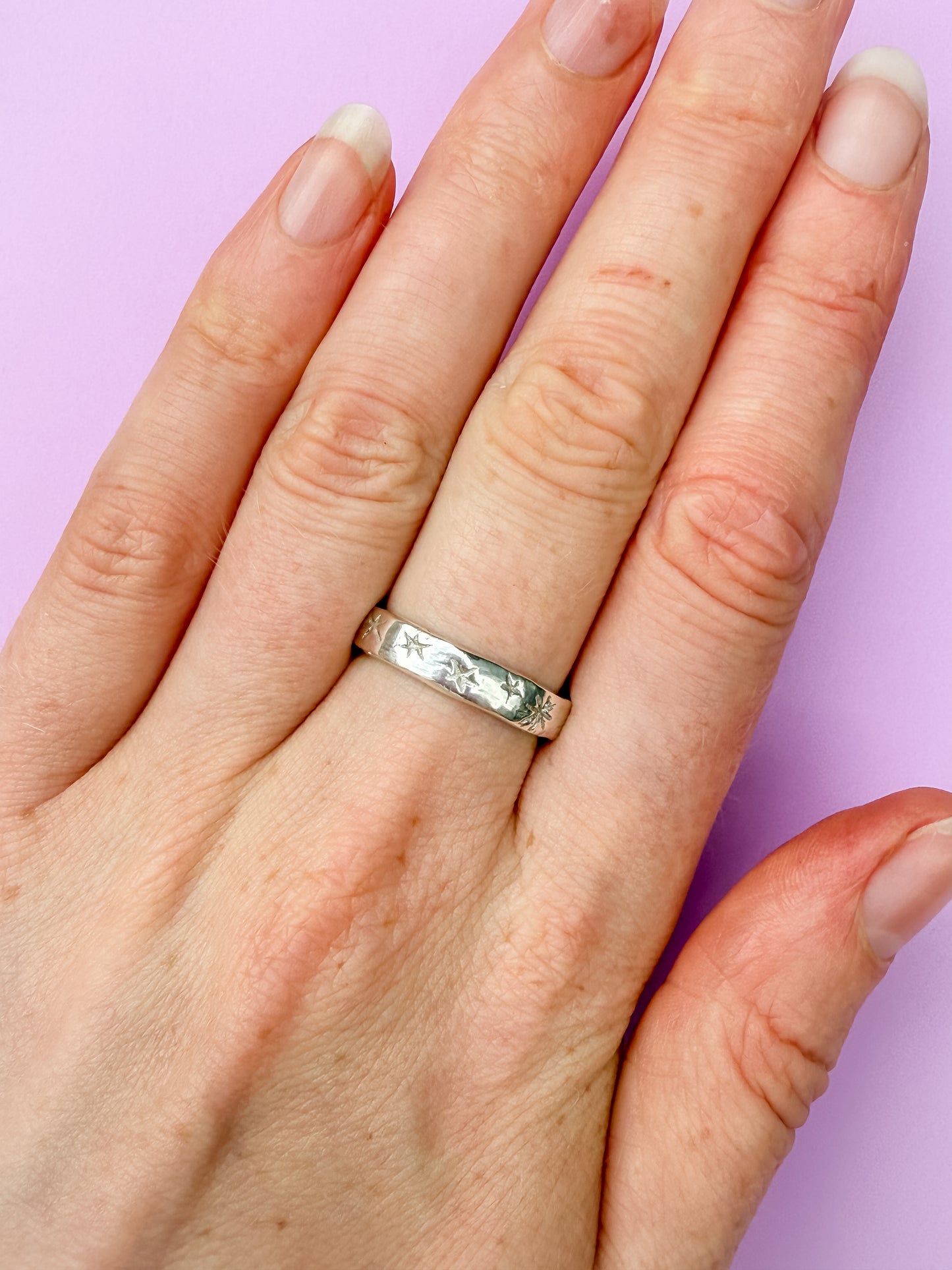 Hand wearing a silver ring on a purple background