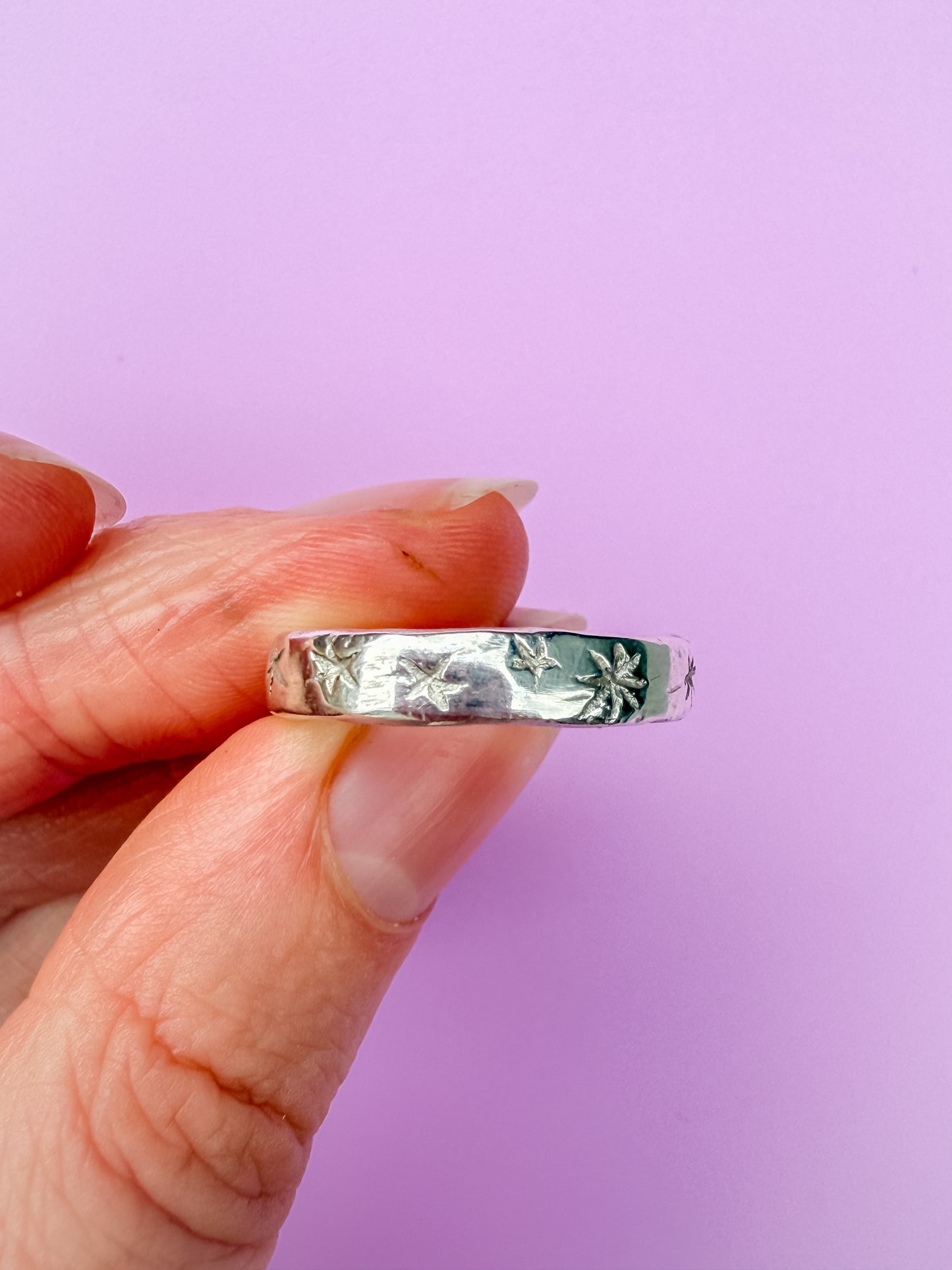Silver ring with etched stars held between fingers against a purple background