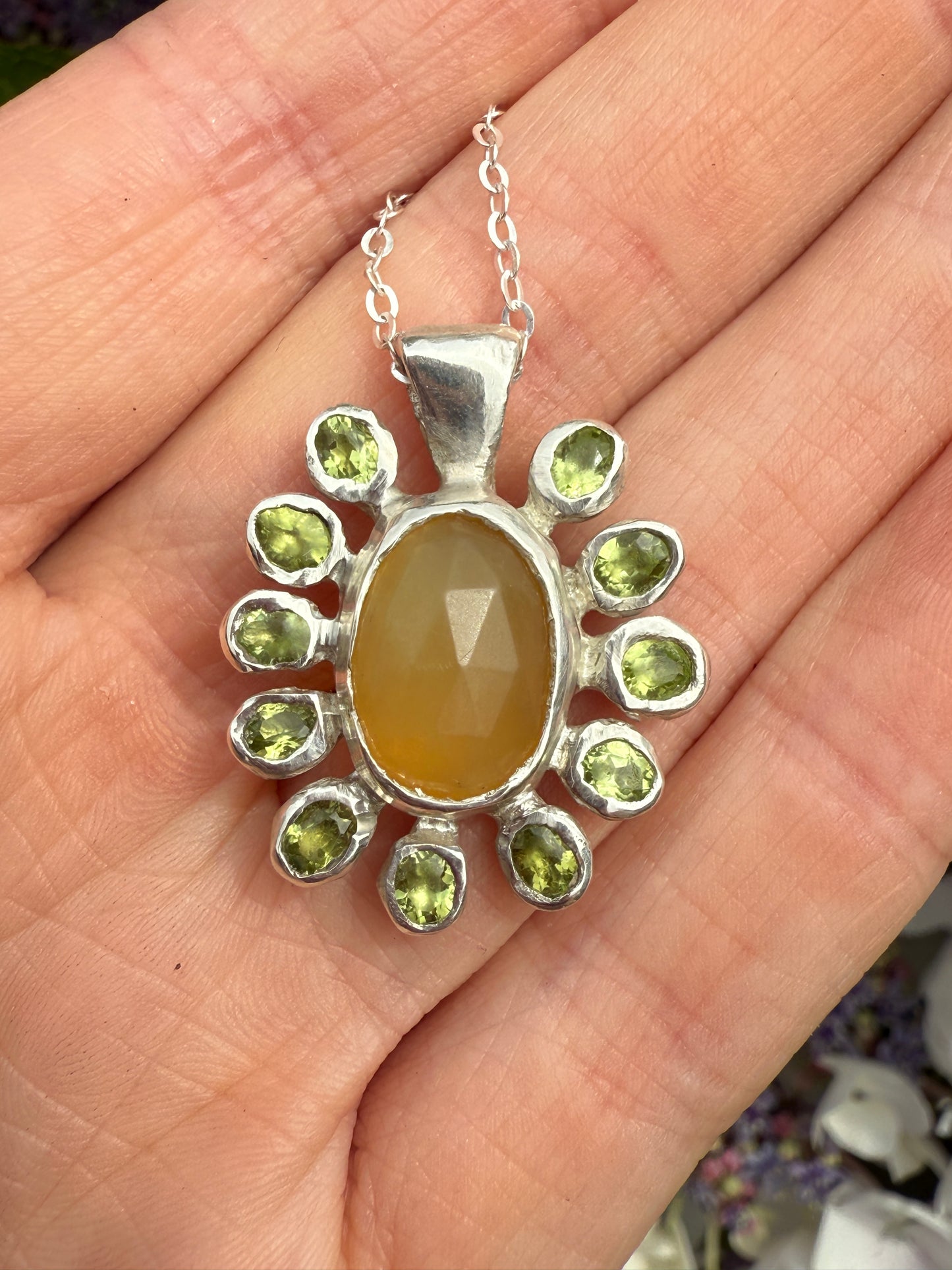 Silver pendant with a yellow center stone and green accents held in a hand.