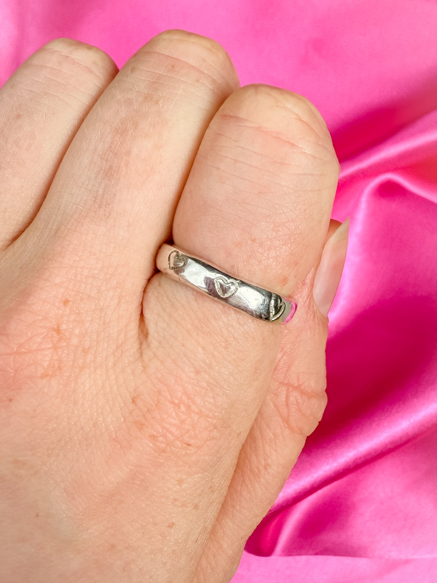 Hand wearing a silver ring with heart design on pink fabric background