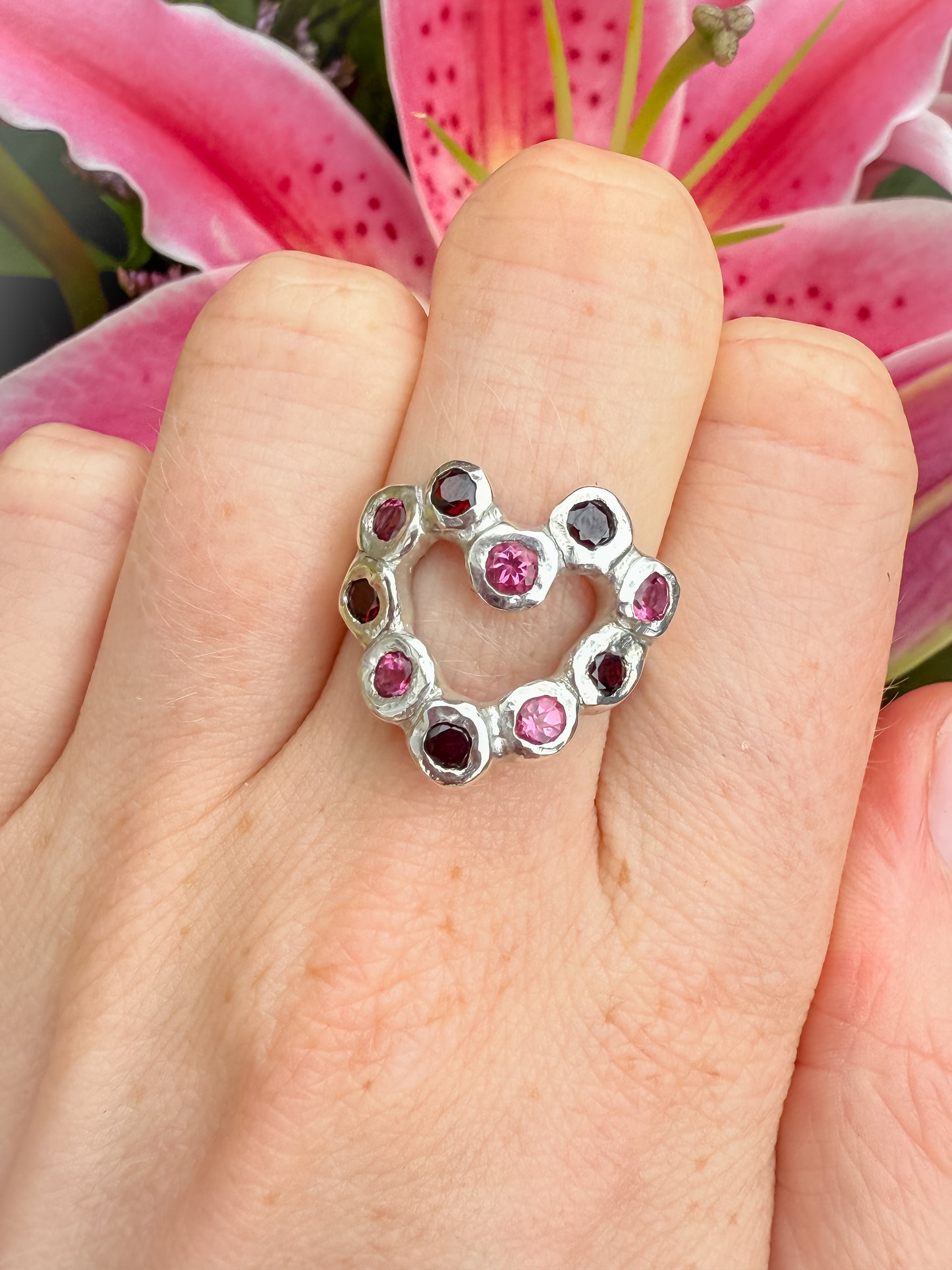 Silver heart ring with pink and red gemstones against lily flower