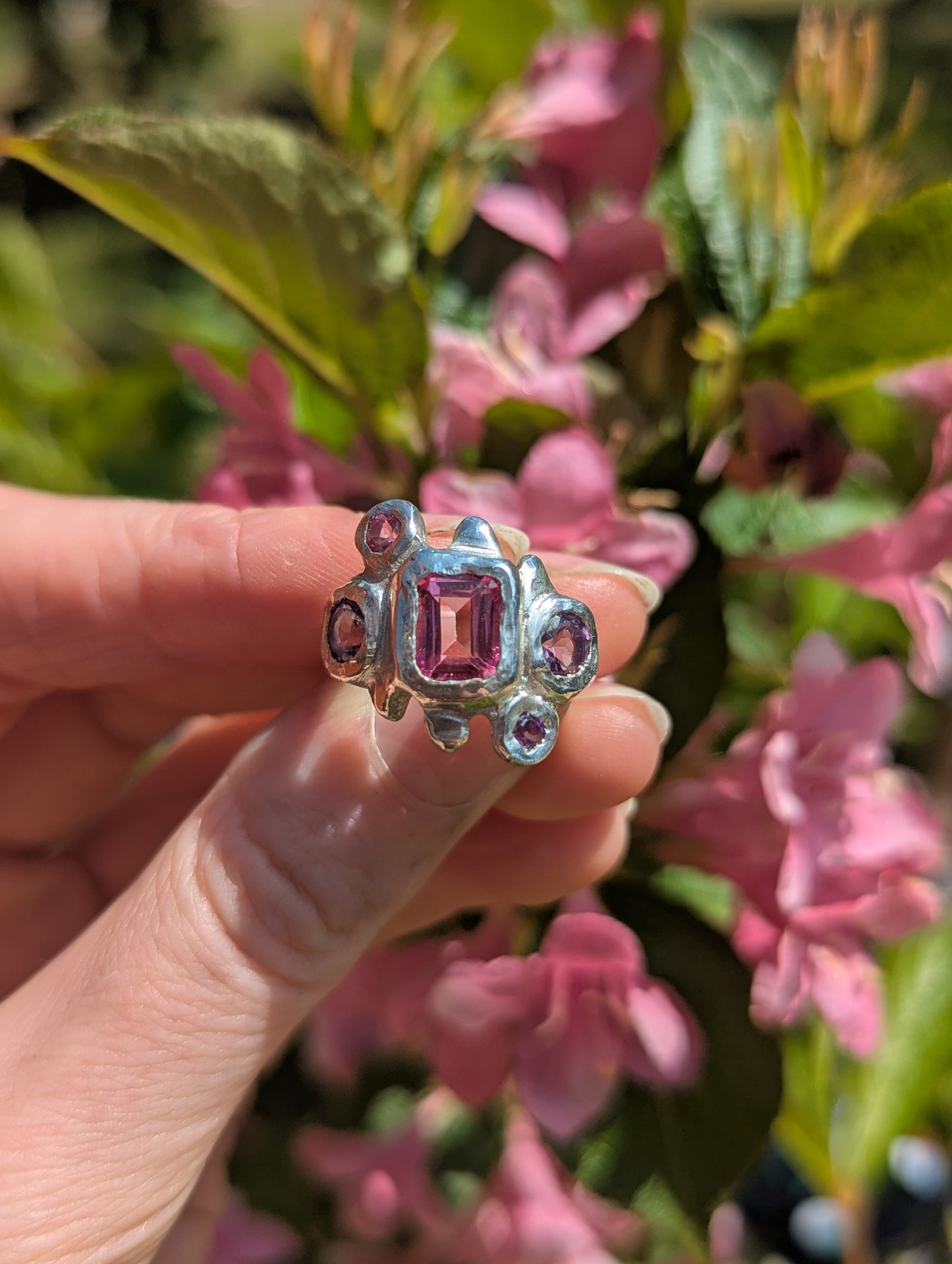 Silver Bohemian Ring with pink and purple gemstones held by a hand against a floral background