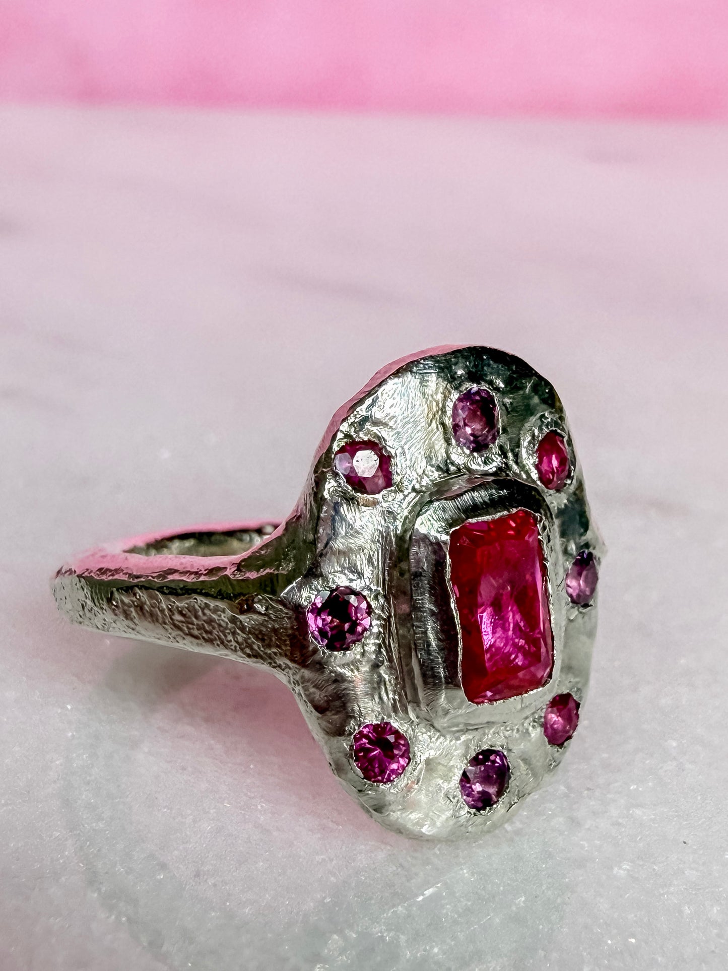 Lab ruby, rhodolite and ruby handmade silver oval ring on marble surface side view