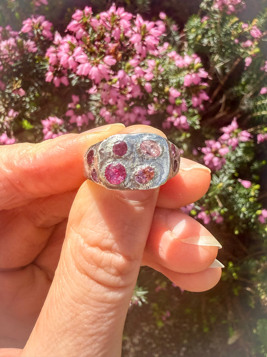 Silver ring with pink gemstones held by a hand against a blurred natural background