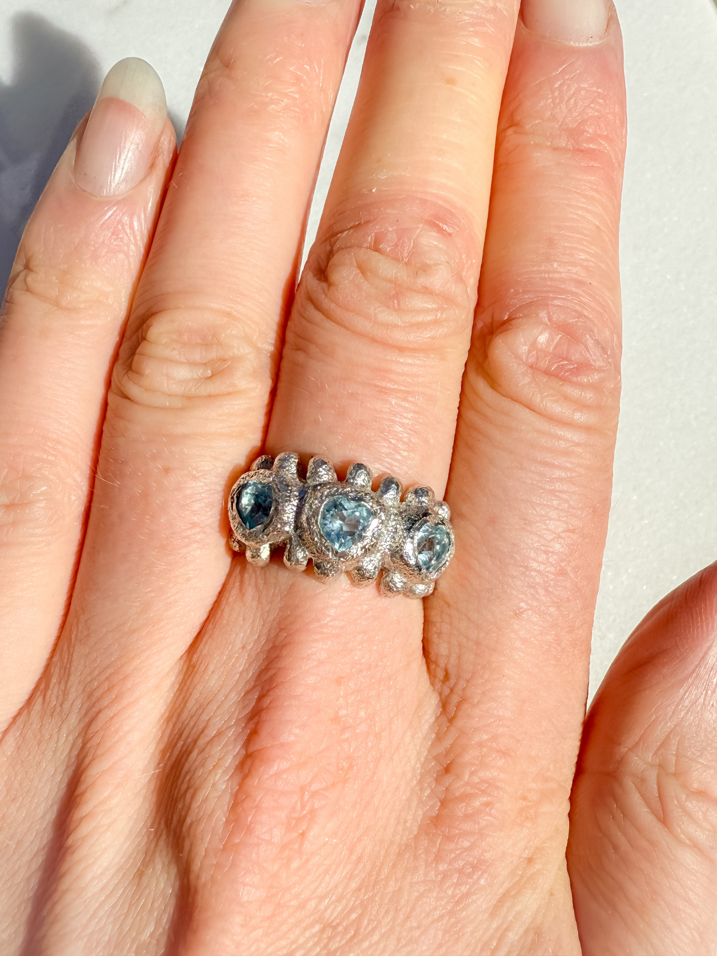 Silver ring with blue gemstones on a hand against a neutral background
