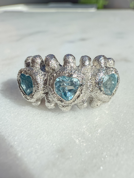 Silver ring with heart-shaped blue gemstones on a white background