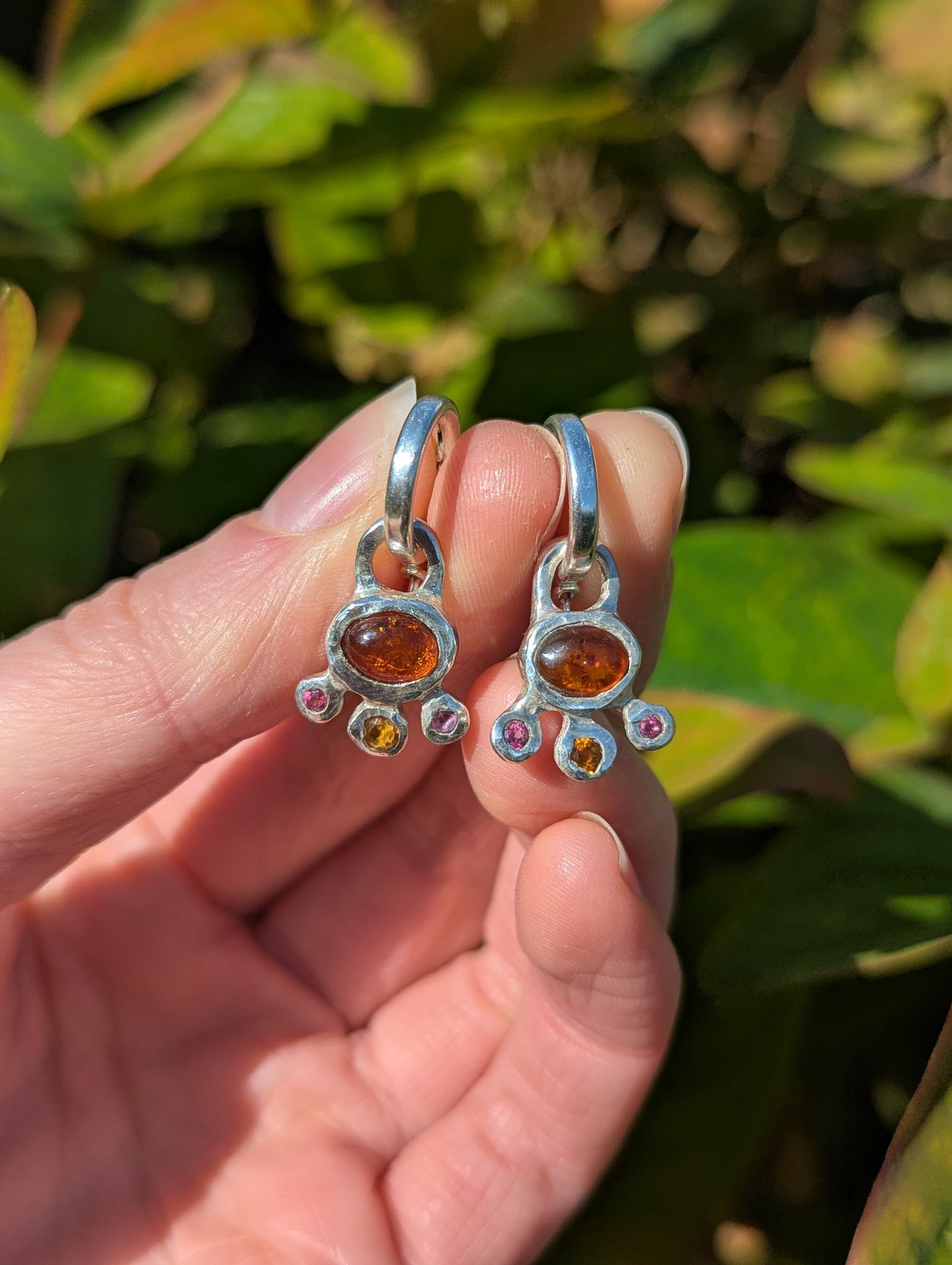Silver earrings with amber stones held between fingers against a green leafy background