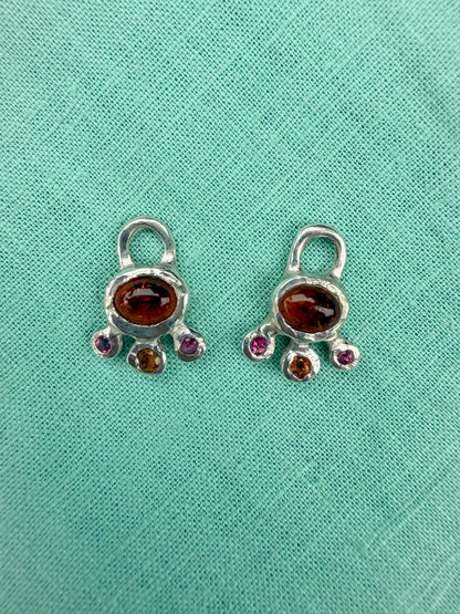 Pair of silver charms with embedded gemstones on a teal fabric background
