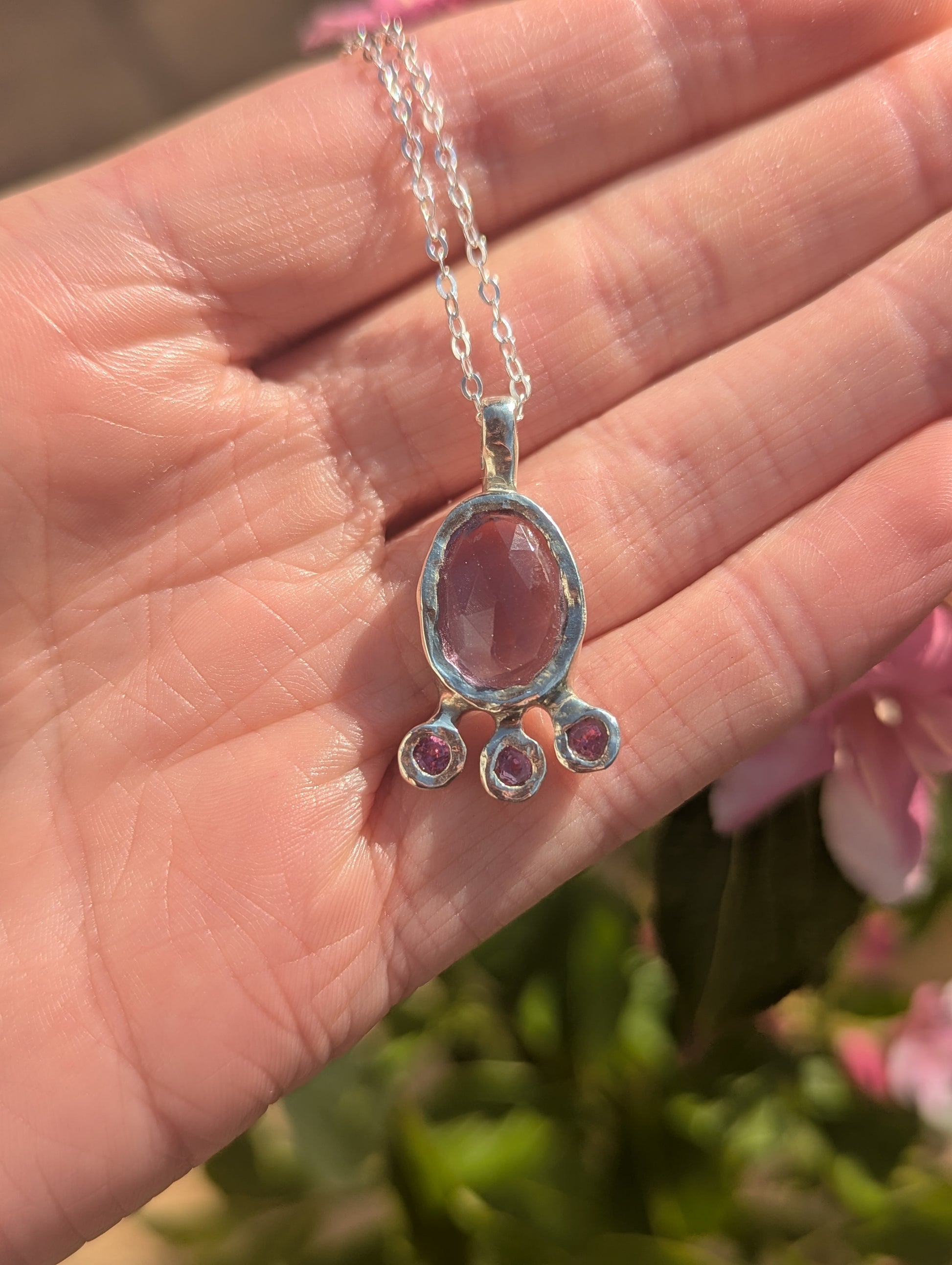 Silver necklace with a pink gemstone pendant held in a hand against a blurred natural background