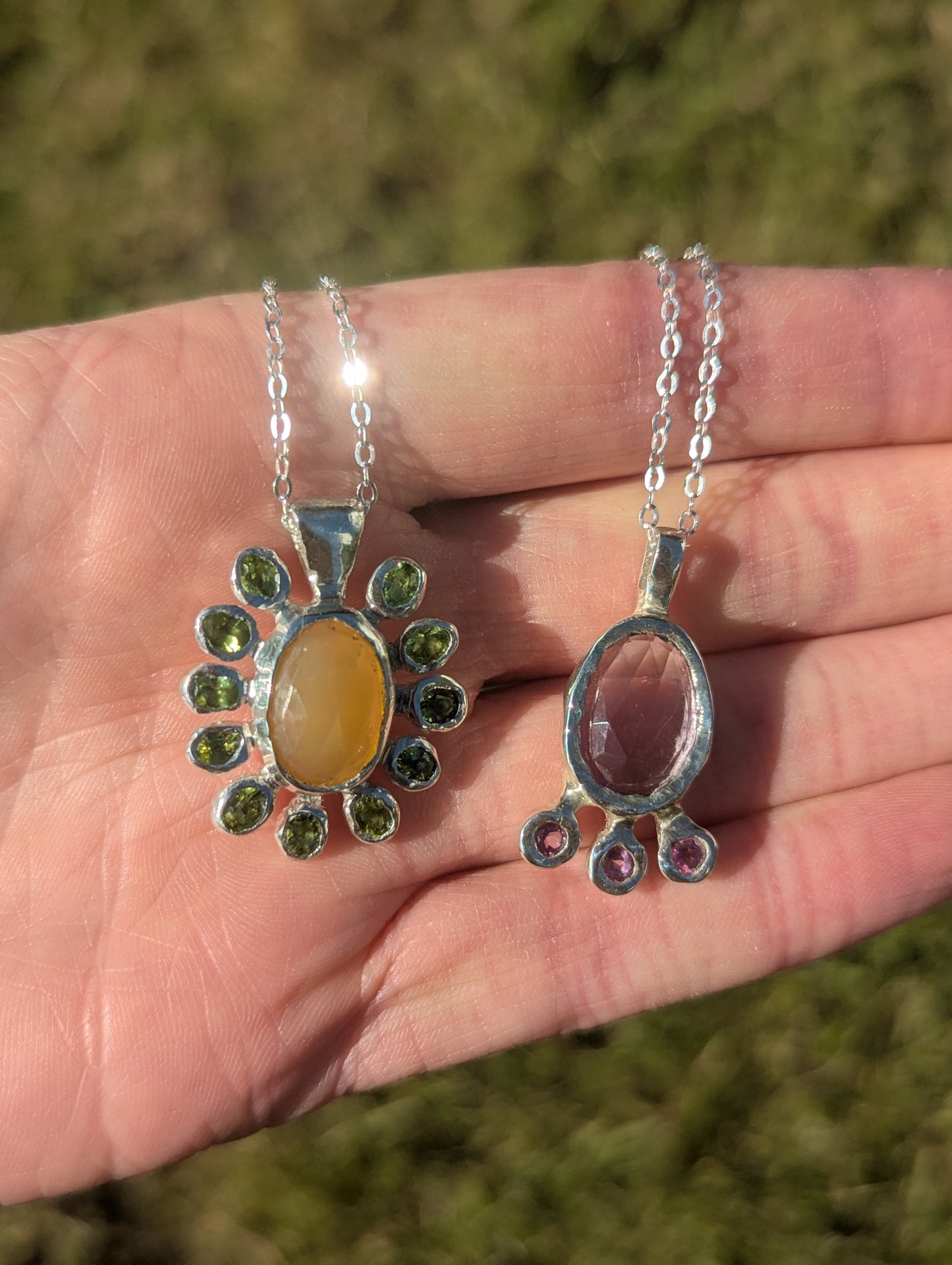 Two silver pendants held in a hand with a grassy background