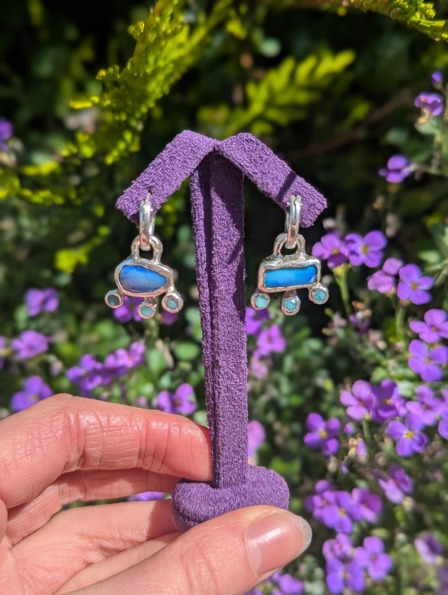 Pair of earrings with blue stones on a purple stand against a floral background