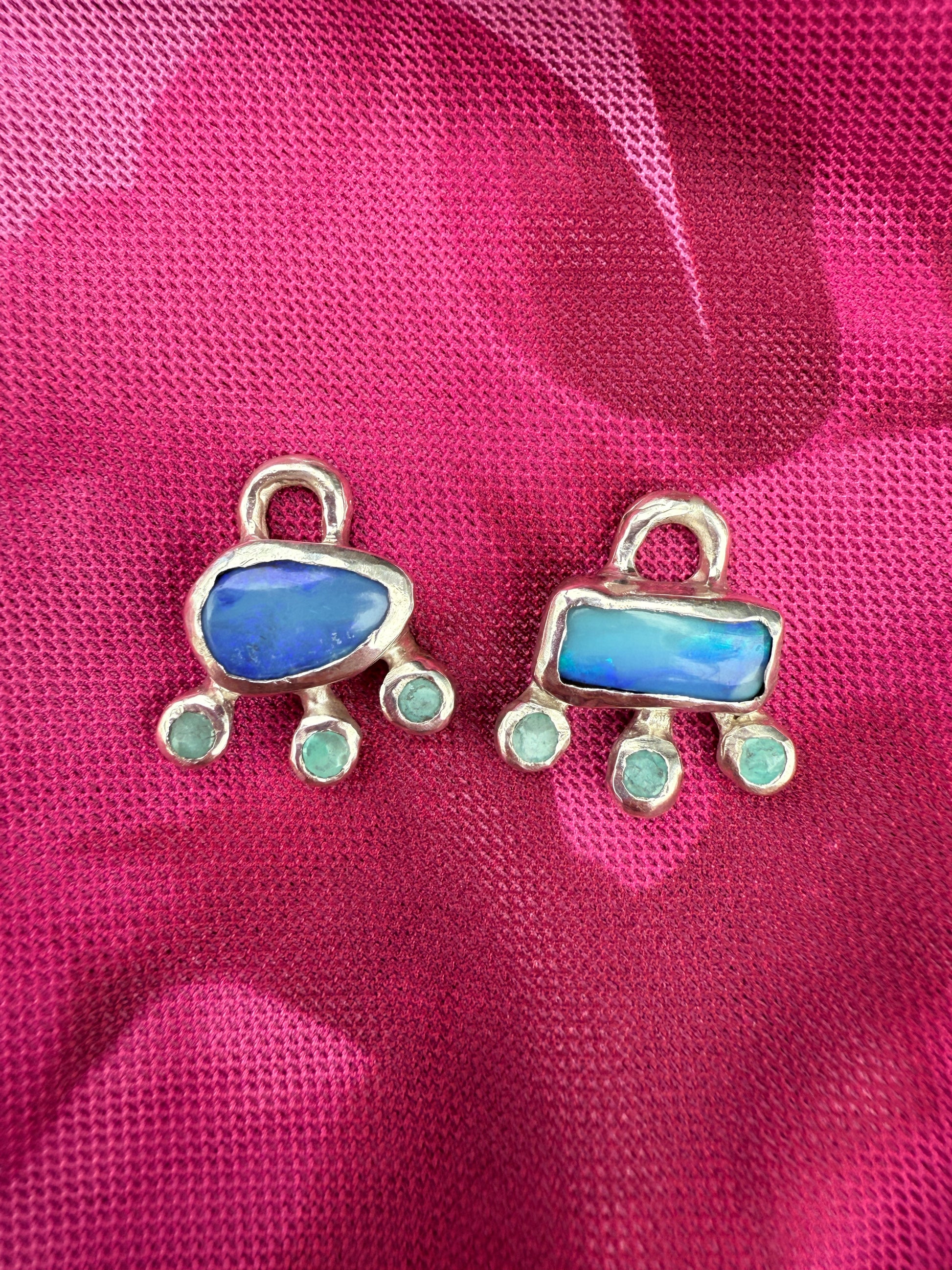Two blue stone pendants with silver frames on a pink fabric background