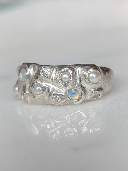Silver ring with embedded pearls, opals and moissanite gemstones on a white background