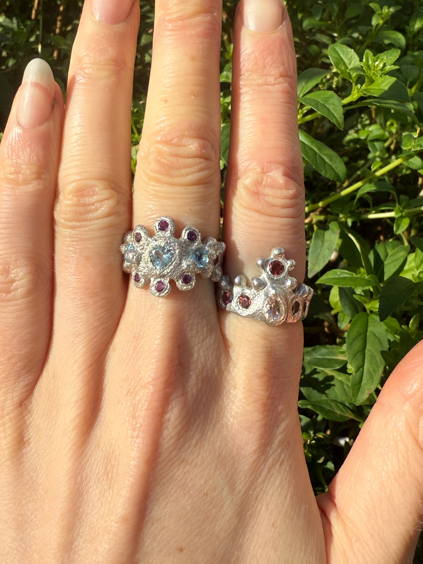 Two silver rings with gemstones on a hand against a green leafy background