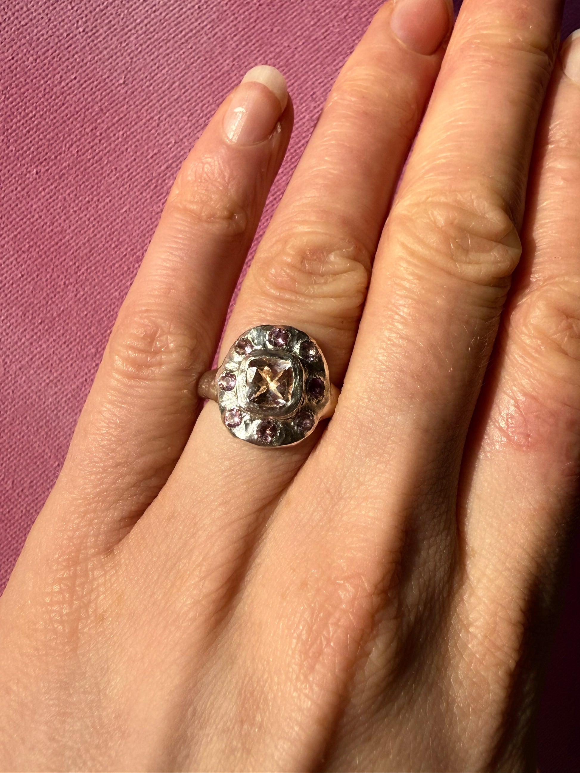 Close up of hand wearing a cushion cut peach morganite pink tourmaline handmade silver ring on pink background