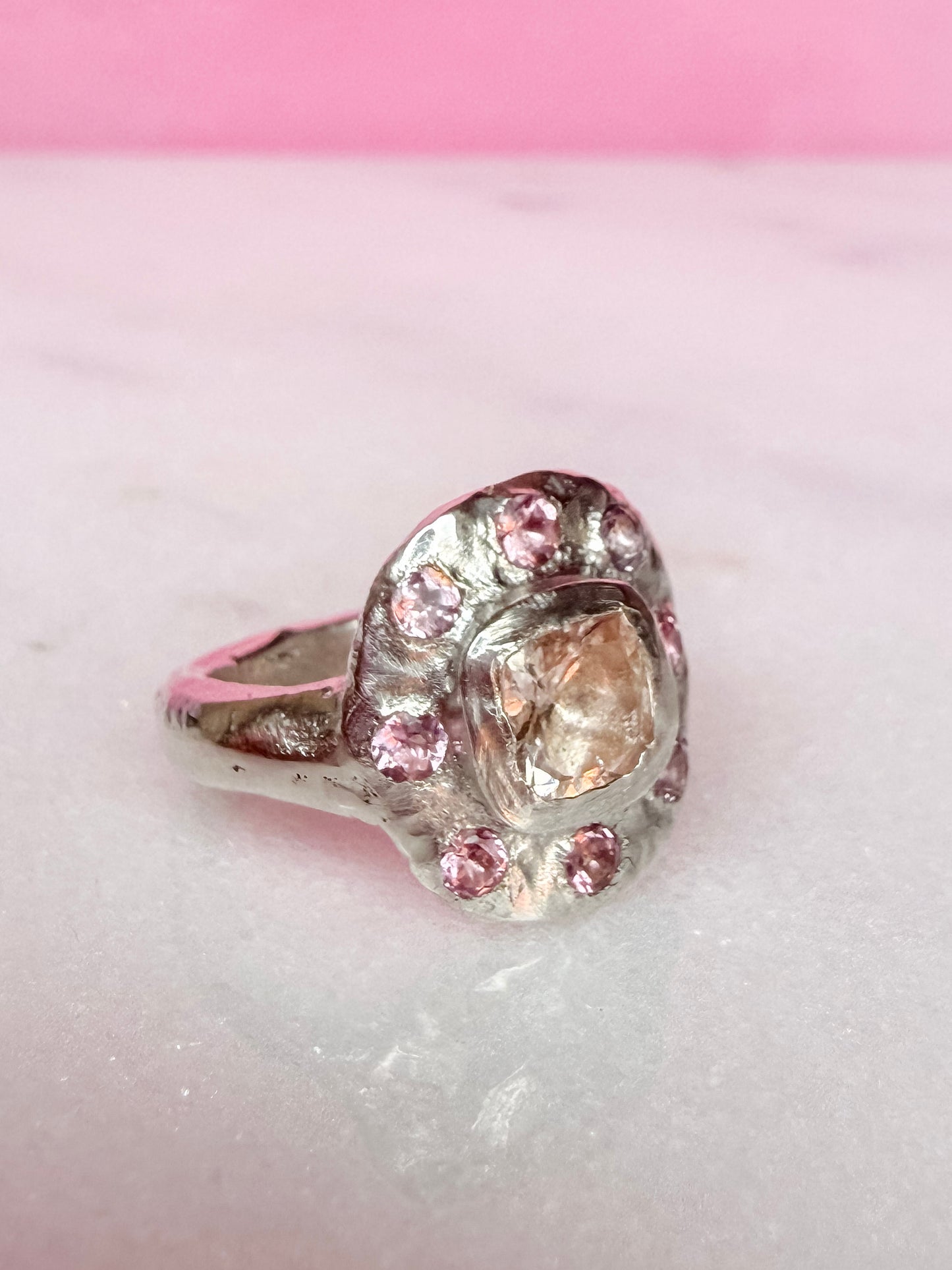 Side view of a cushion cut peach morganite pink tourmaline handmade silver ring on white and pink background 