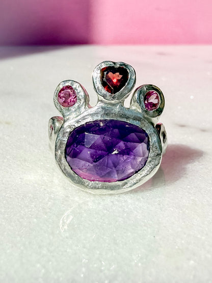 Dark amethyst slice, garnet heart, pink topaz and ruby handmade silver ring on marble surface