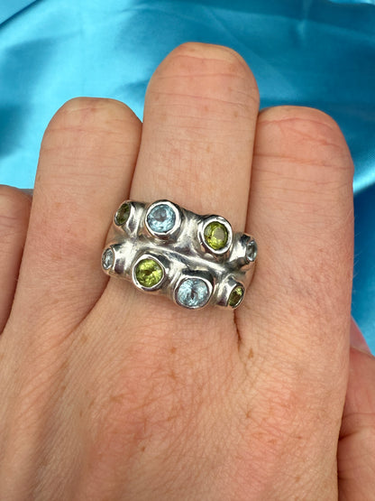 Silver ring with blue and green stones on a hand against a blue background