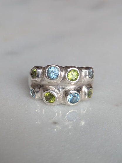 Silver ring with green and blue gemstones on a light gray background
