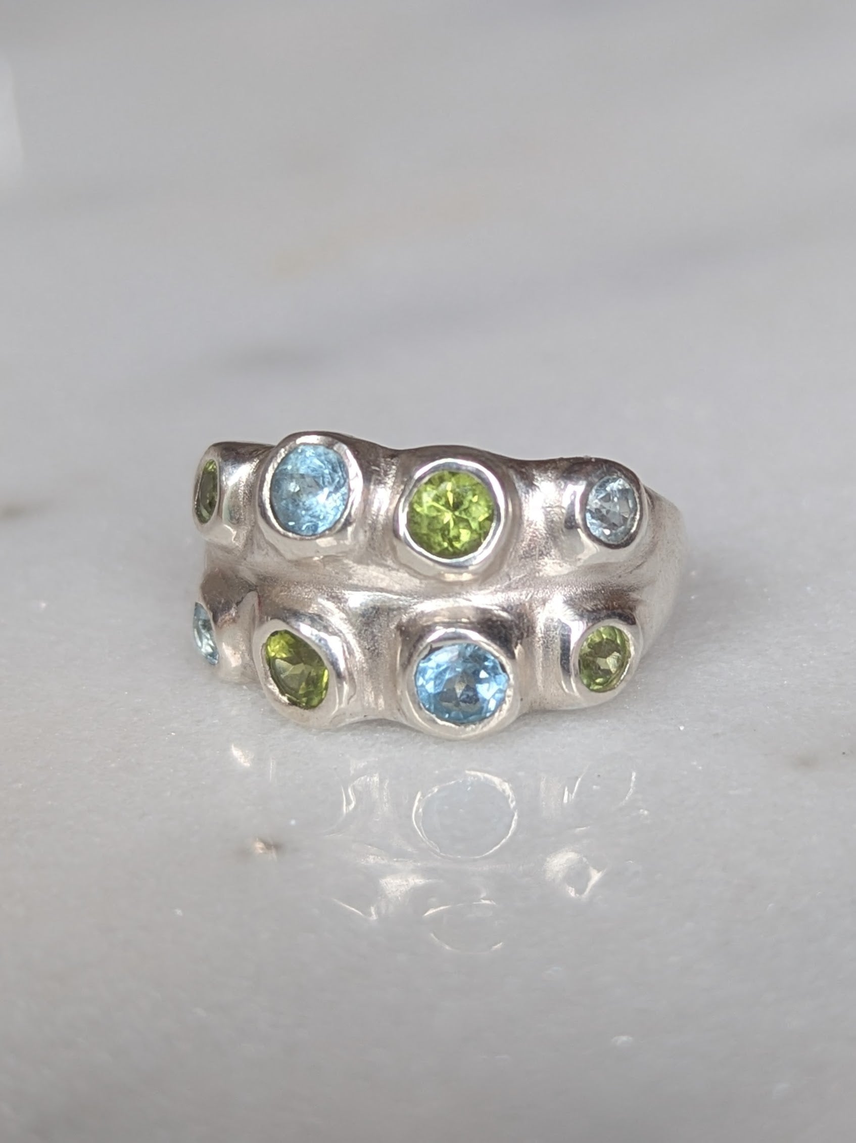 Silver ring with blue and green gemstones on a white background